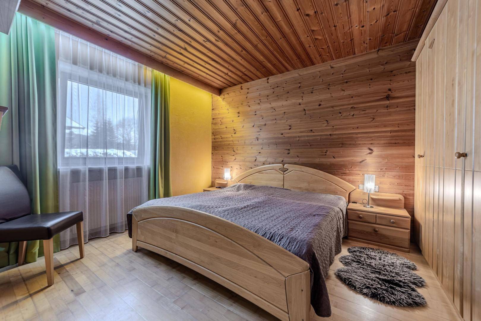 Rustikales Schlafzimmer mit Holzvertäfelung an Wänden und Decke sowie einem großen Fenster.