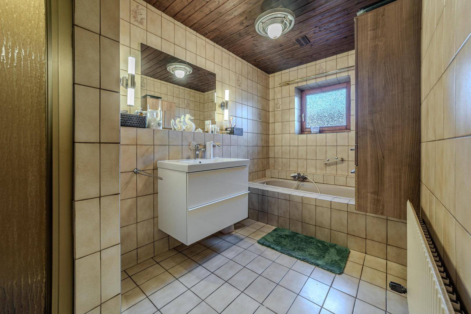 Badezimmer mit beigefarbenen Fliesen, Badewanne, modernem Waschtisch und Holzdecke.