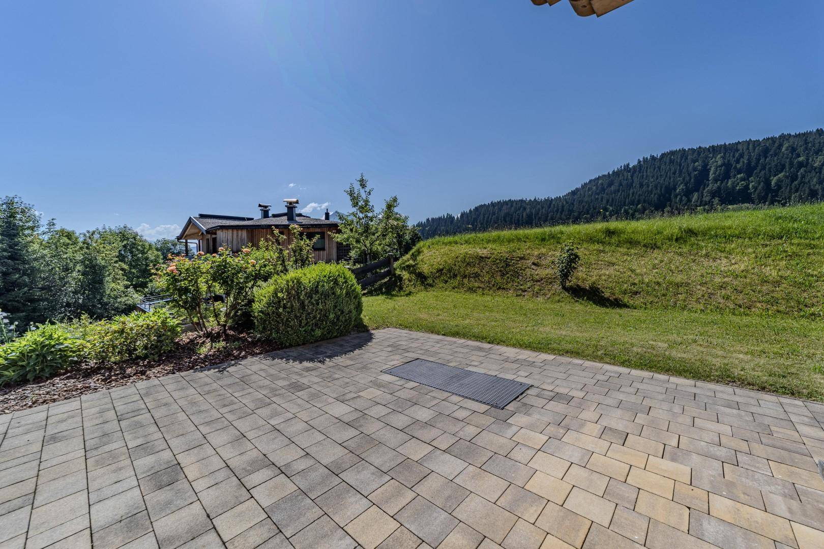 Weitläufige gepflasterte Terrasse mit angrenzender Rasenfläche und Bergblick.