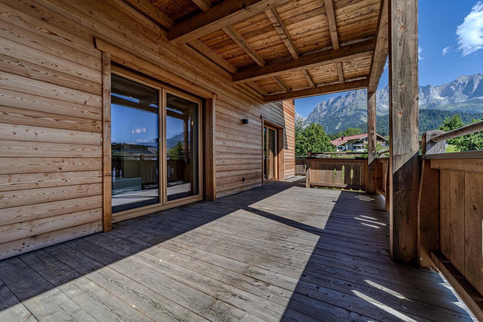 Geräumiger Holzbalkon mit großen Schiebetüren und Panoramablick auf die Berge.