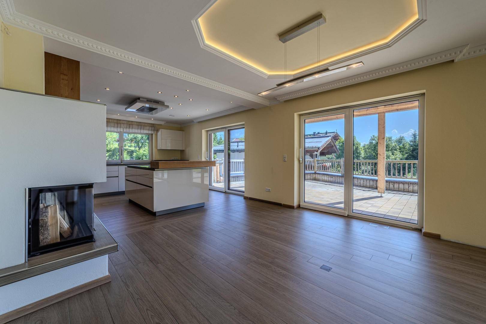 Heller Wohnbereich mit offener Küche, Kamin und Zugang zur großen Terrasse.