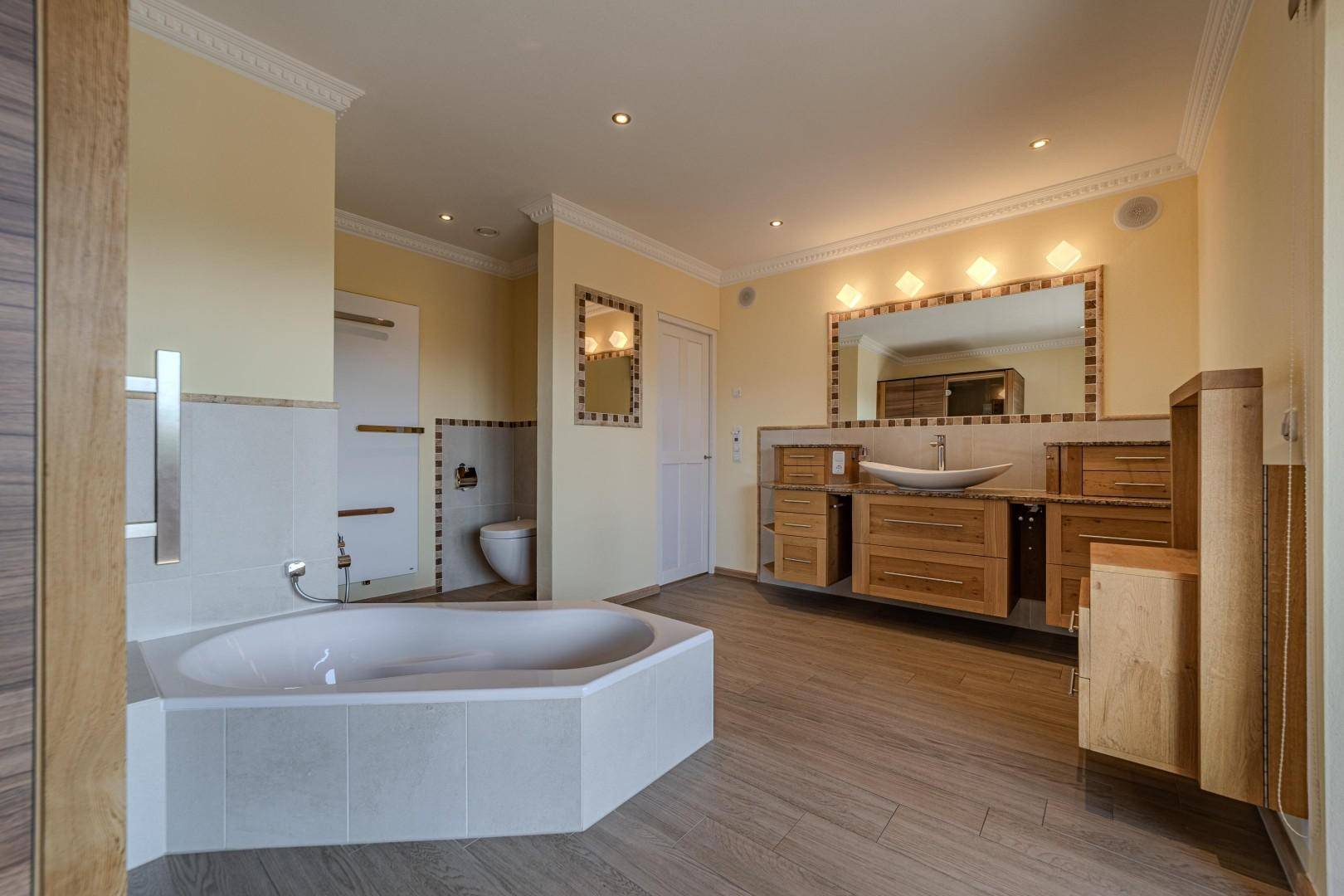 Geräumiges Badezimmer mit Eckbadewanne, Doppelwaschtisch und Holzmöbeln in hellem Ambiente.