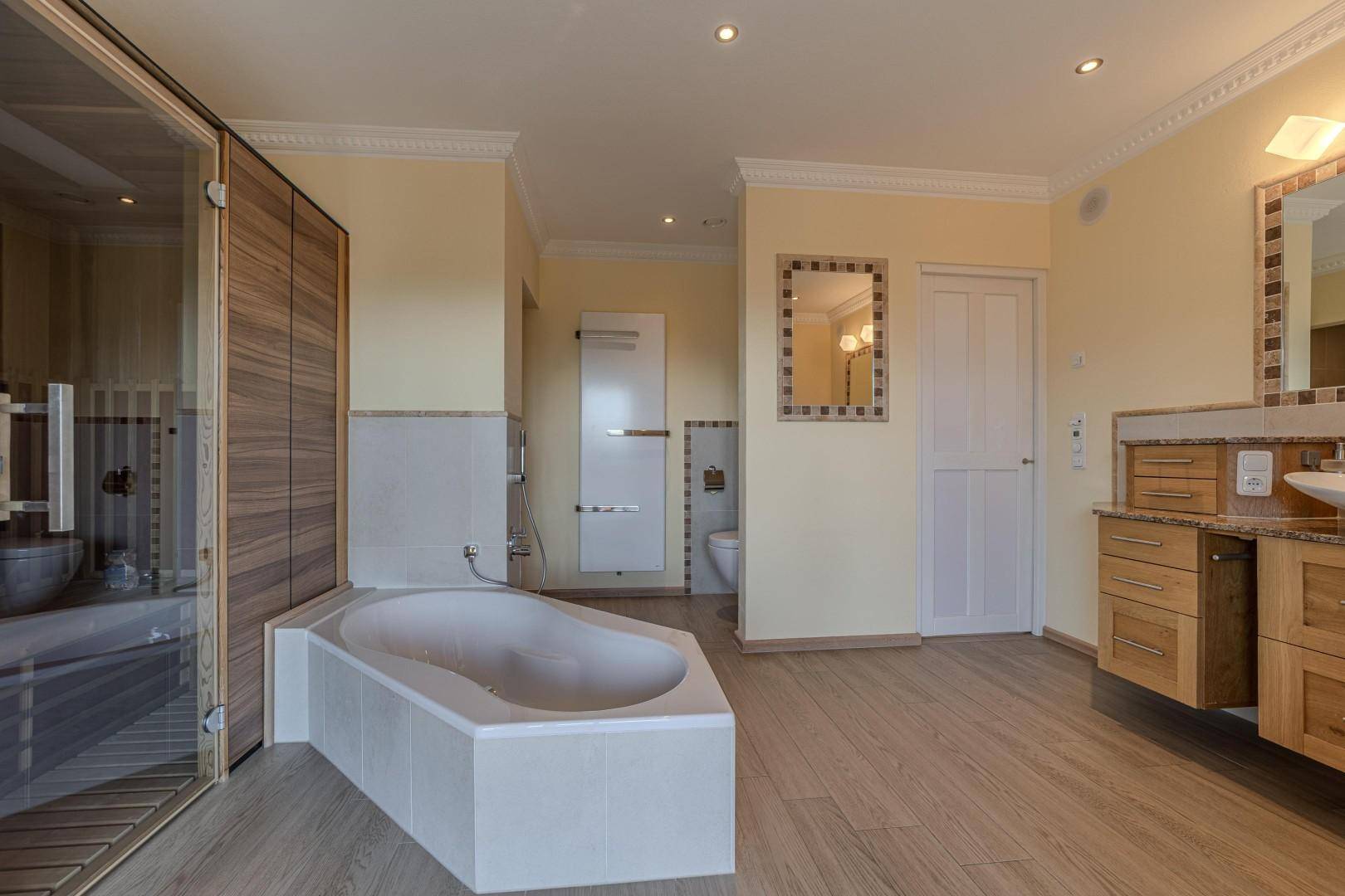 Großes Badezimmer mit Eckbadewanne, Doppelwaschtisch und integrierter Sauna für Wellness.