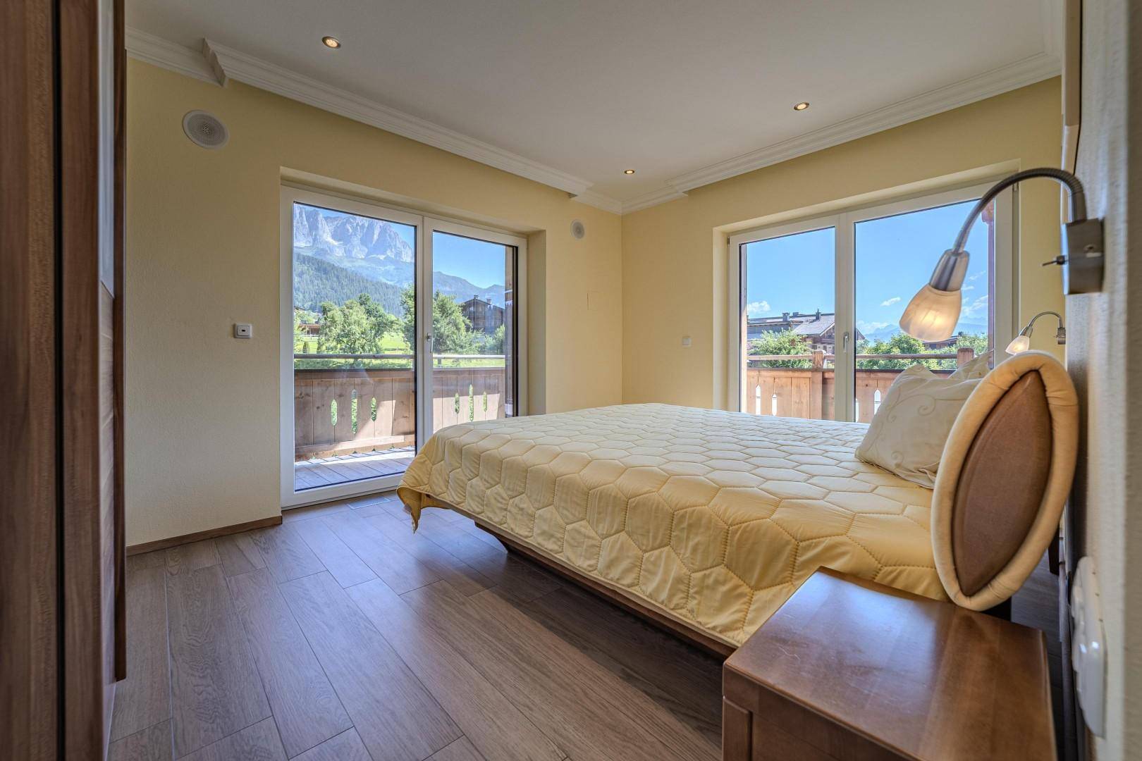 Gemütliches Schlafzimmer mit Doppelbett, Holzboden und Zugang zum Balkon mit Bergblick.