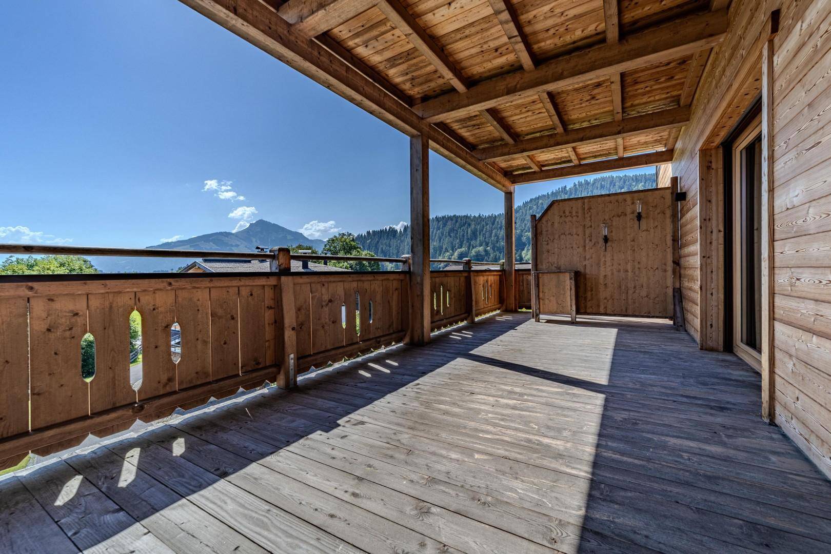 Großer Holzbalkon mit Bergblick und traditioneller Holzverkleidung unter blauem Himmel.