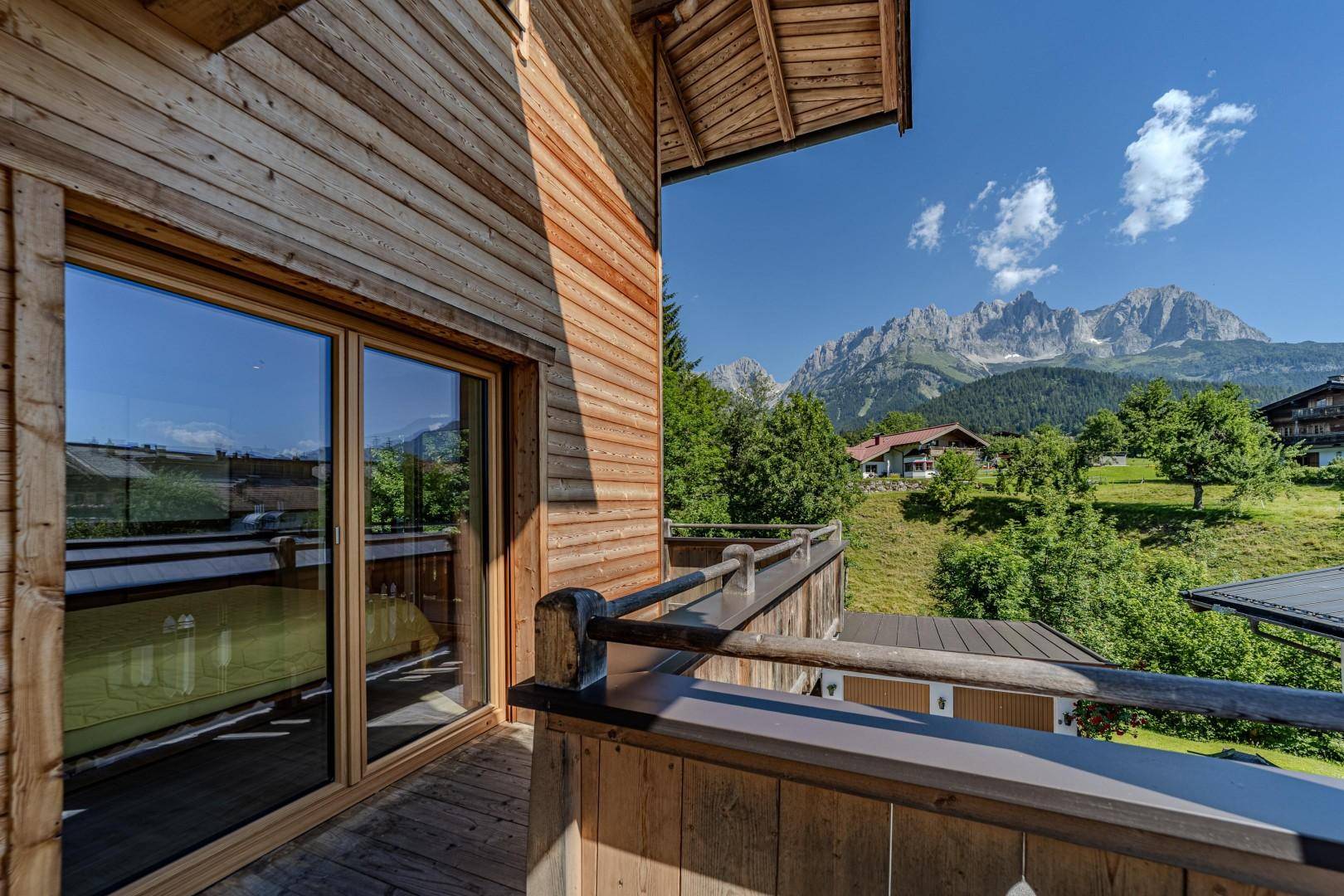 Sonniger Holzbalkon mit weitem Bergblick und großen Fenstern zum Innenraum.