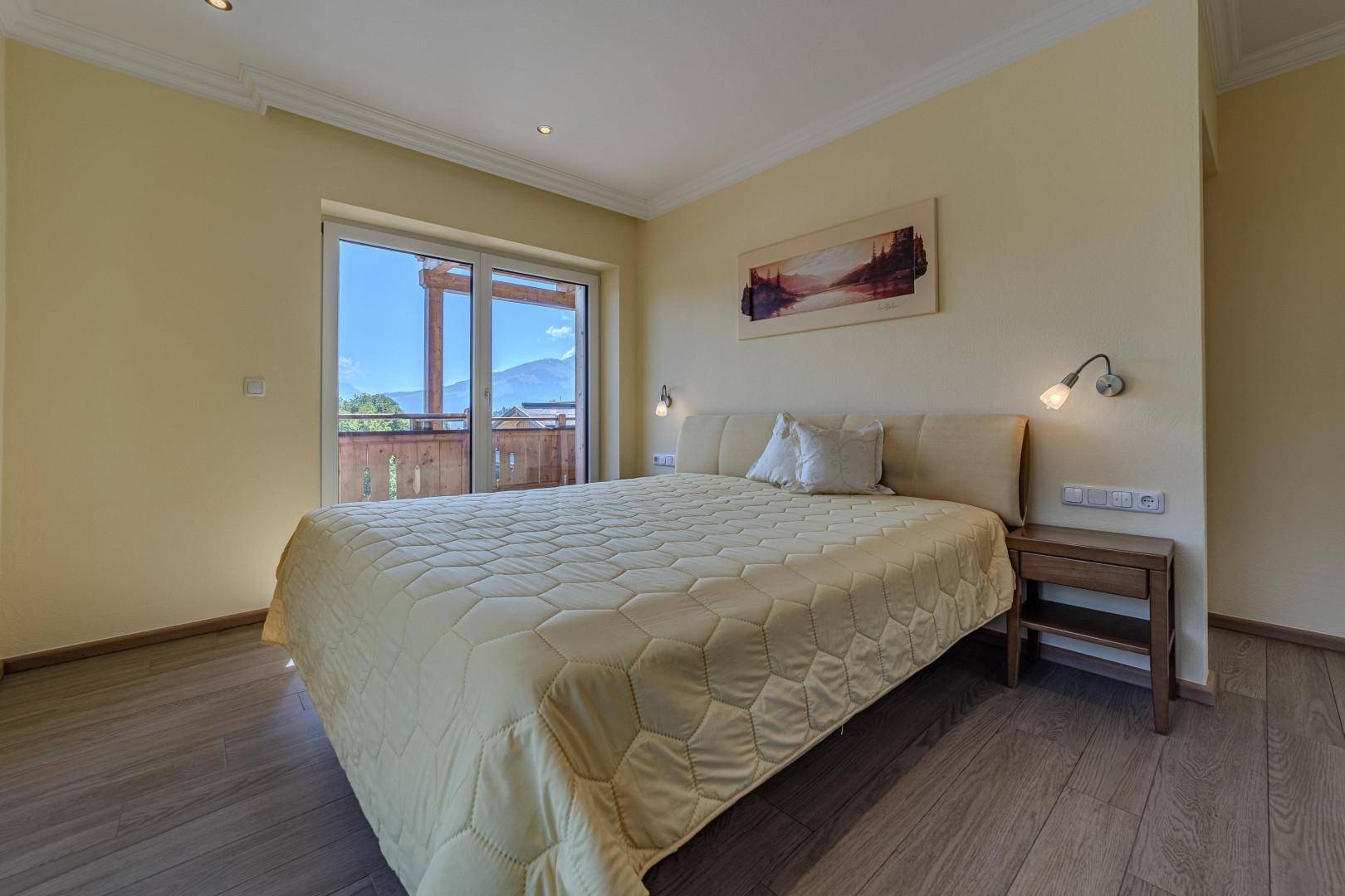 Helles Schlafzimmer mit Doppelbett, Holzboden und Balkonzugang mit Bergblick.