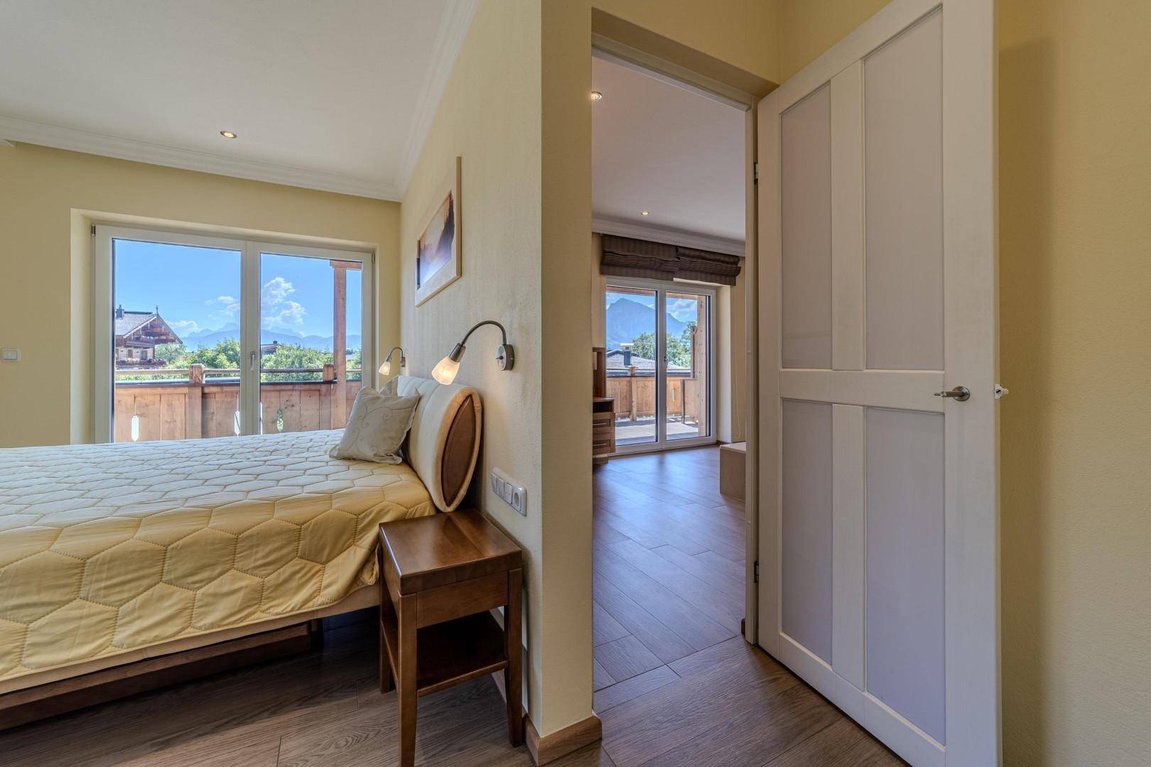 Schlafzimmer mit Holzboden und Blick in einen angrenzenden Raum mit Balkonzugang.