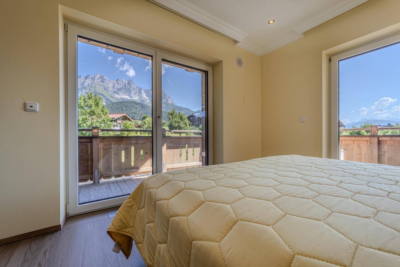Schlafzimmer mit Doppelbett, Holzboden und beeindruckendem Bergblick vom Balkon.