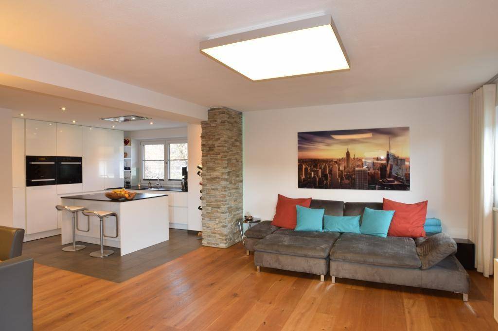 Geräumiges Wohnzimmer mit großer Couch, Holzboden und Blick auf die offene Küche.