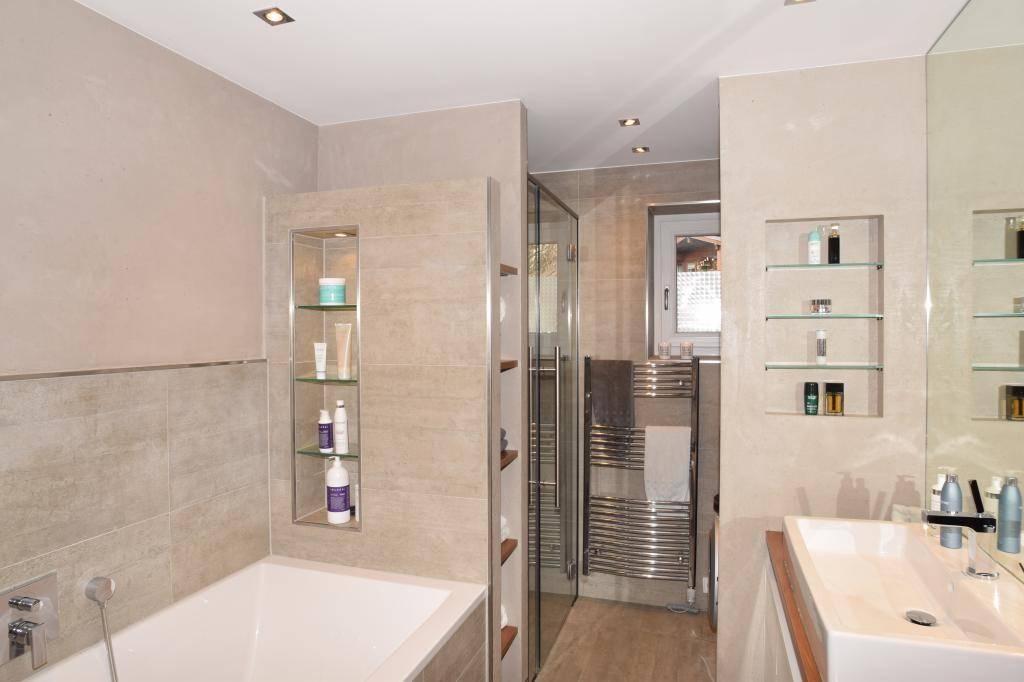 Modernes Badezimmer mit Badewanne, Dusche, beheiztem Handtuchhalter und Fenster.