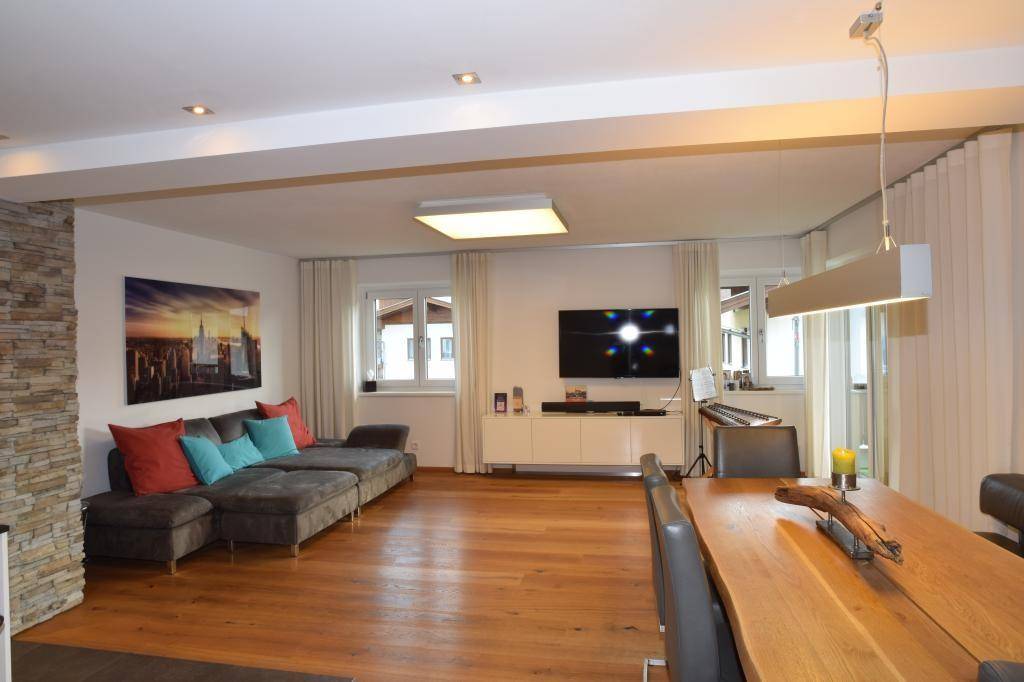 Heller Wohn- und Essbereich mit Fernseher, Holzboden und Zugang zu weiteren Räumen.