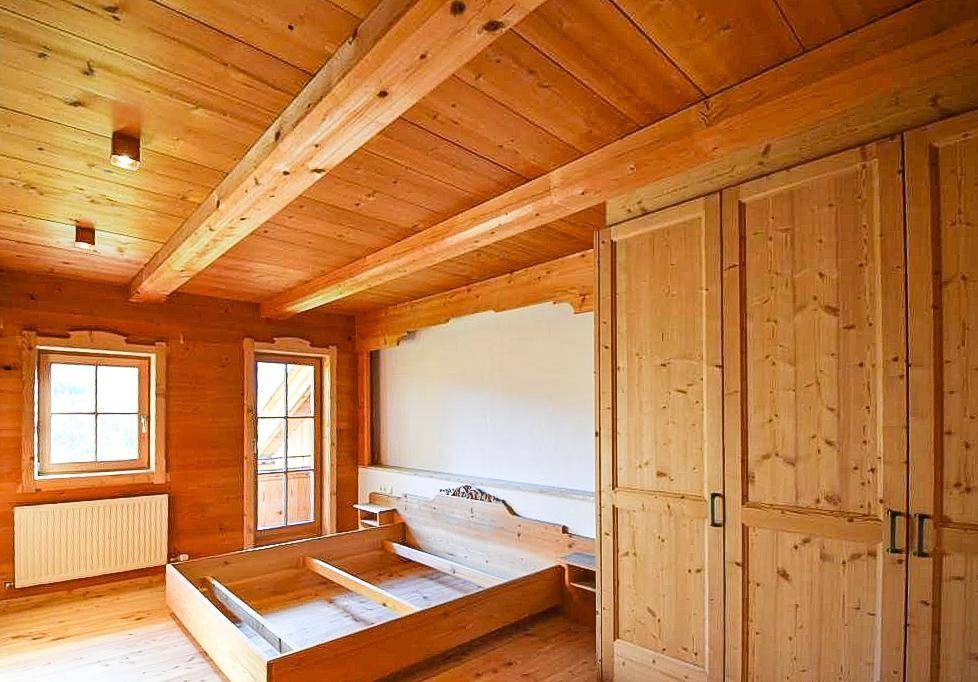 Schlafzimmer mit Holzbalkendecke, Holzboden und Zugang zu einem kleinen Balkon.