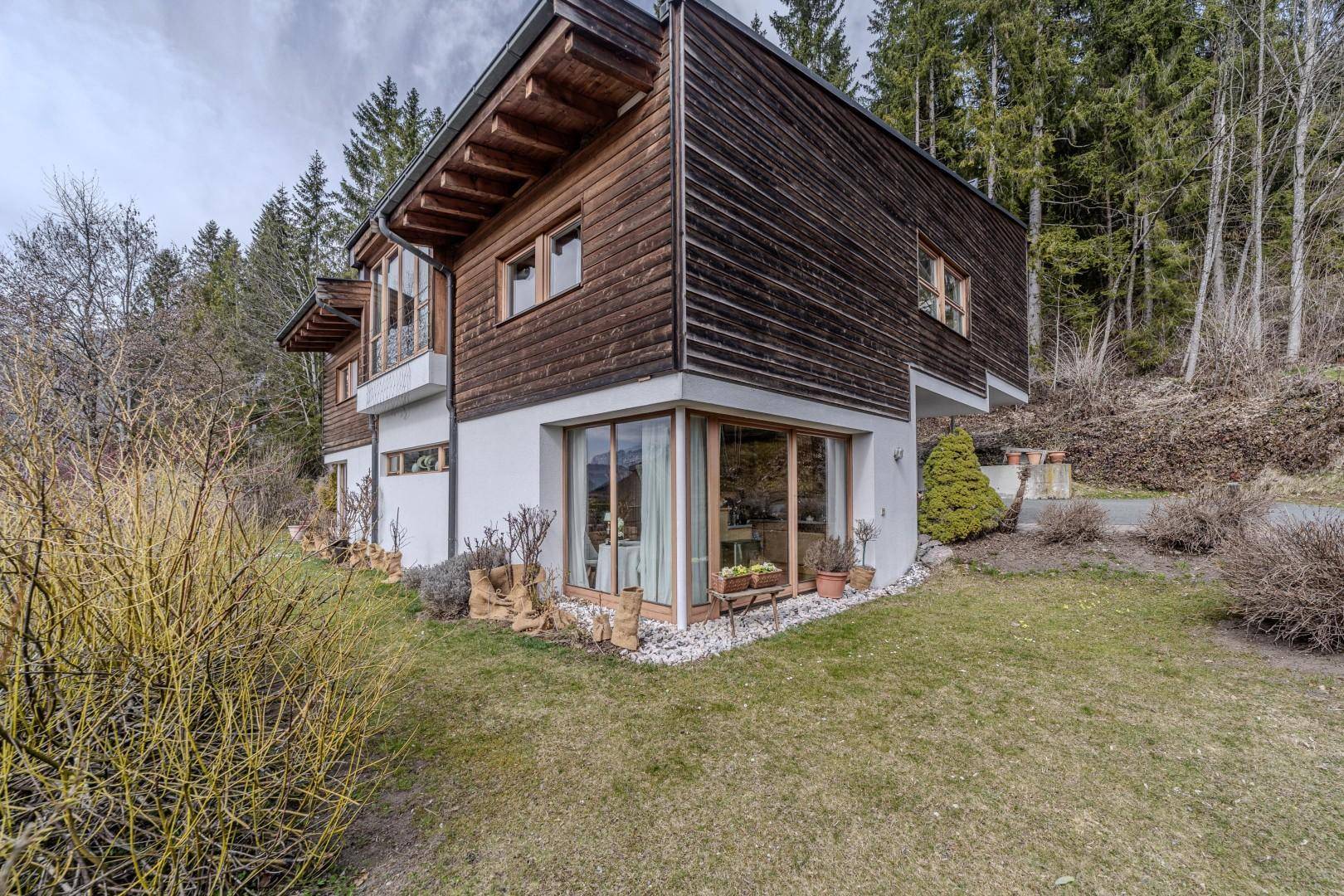 Seitenansicht des Hauses mit Holzfassade, großen Fenstern und gepflegtem Gartenbereich.