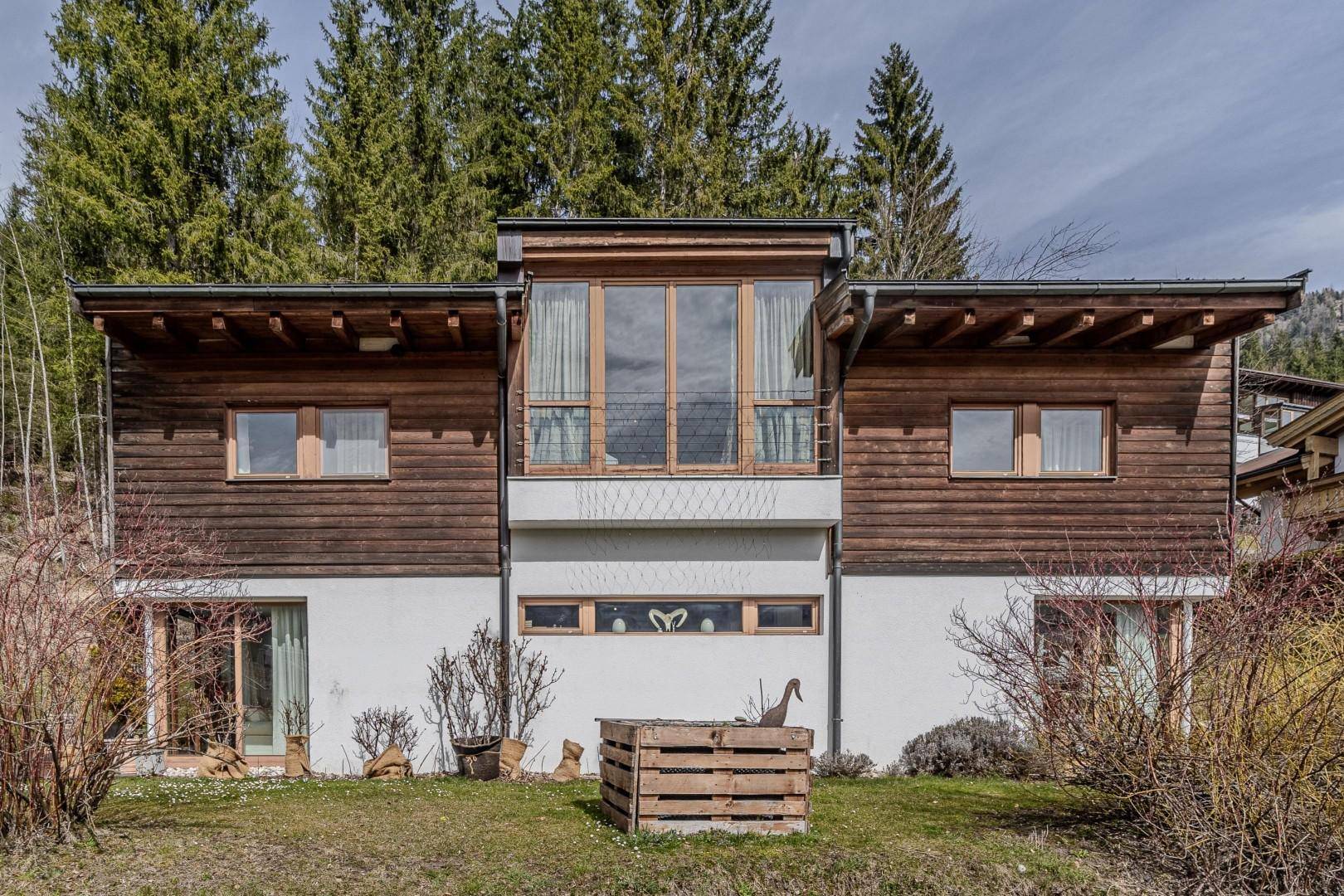 Moderne Fassade des Hauses mit Holz- und Weißtönen, großen Fenstern und umgebendem Garten.