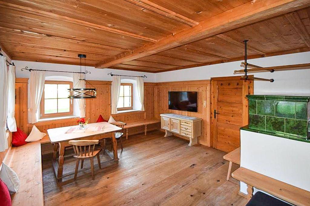 Traditionelles Wohnzimmer mit Holzboden, Kachelofen und gemütlicher Sitzecke unter Holzbalkendecke.