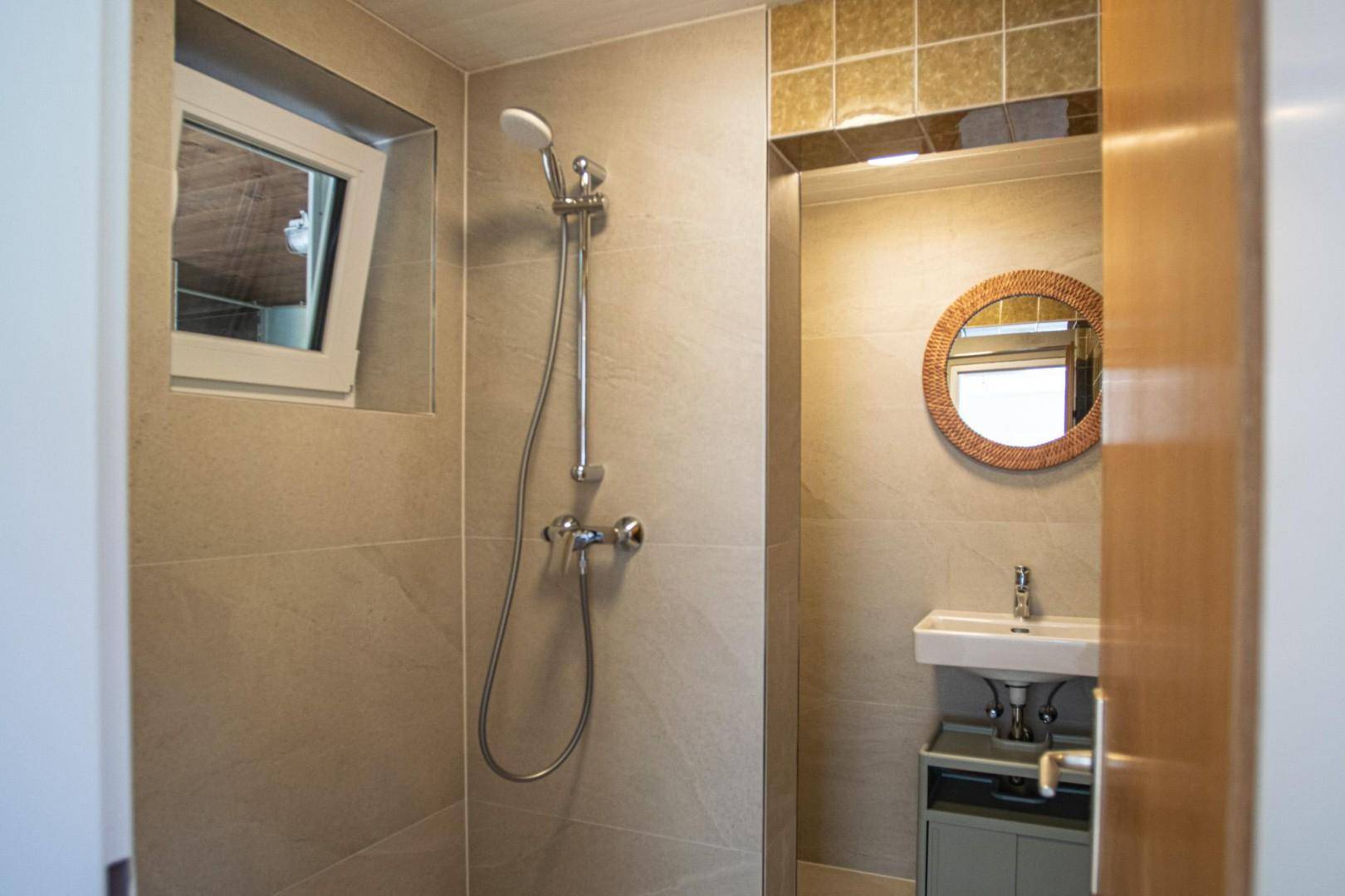 Modernes Badezimmer mit beigefarbenen Fliesen, Duschbereich und kleinem Waschbecken.