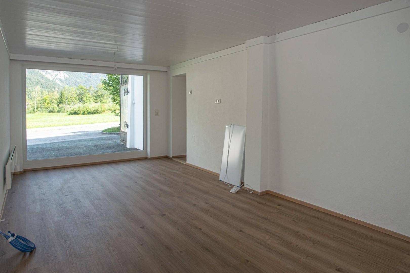 Heller Raum mit Laminatboden und großer Öffnung zum Außenbereich mit grüner Aussicht.