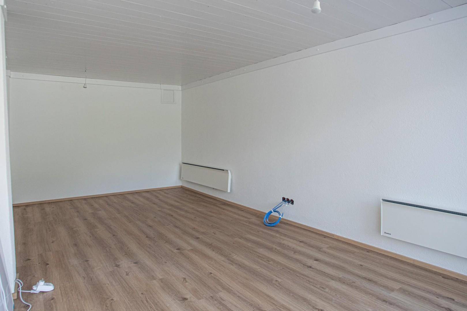 Leerer Raum mit Laminatboden, weißen Wänden und Decken sowie Heizkörpern an den Wänden.