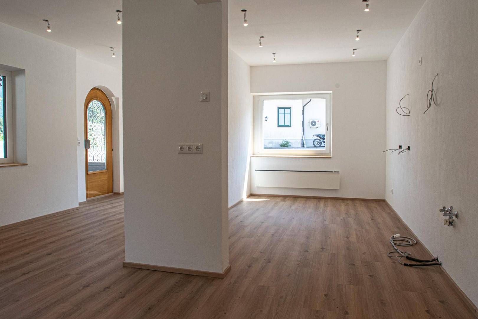 Heller, offener Raum mit Laminatboden, weißen Wänden und mehreren Fenstern für viel Tageslicht.
