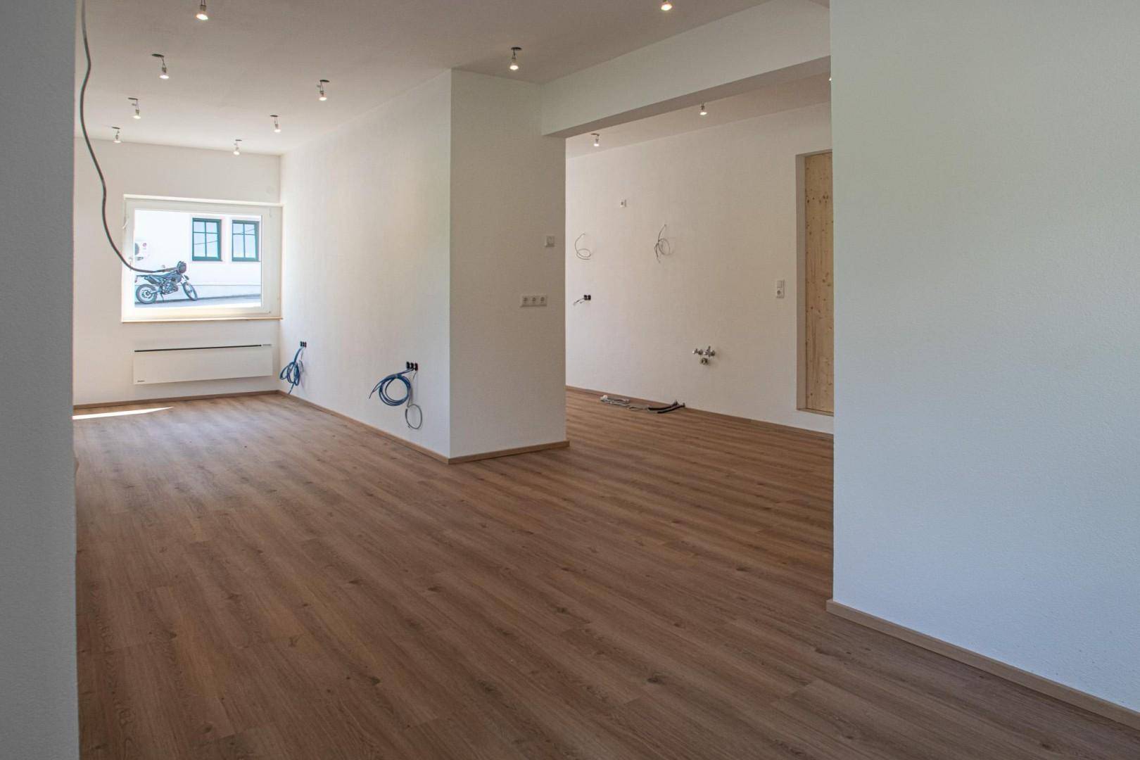 Geräumiger, heller Raum mit Laminatboden, weißen Wänden und sichtbaren Elektroinstallationen.