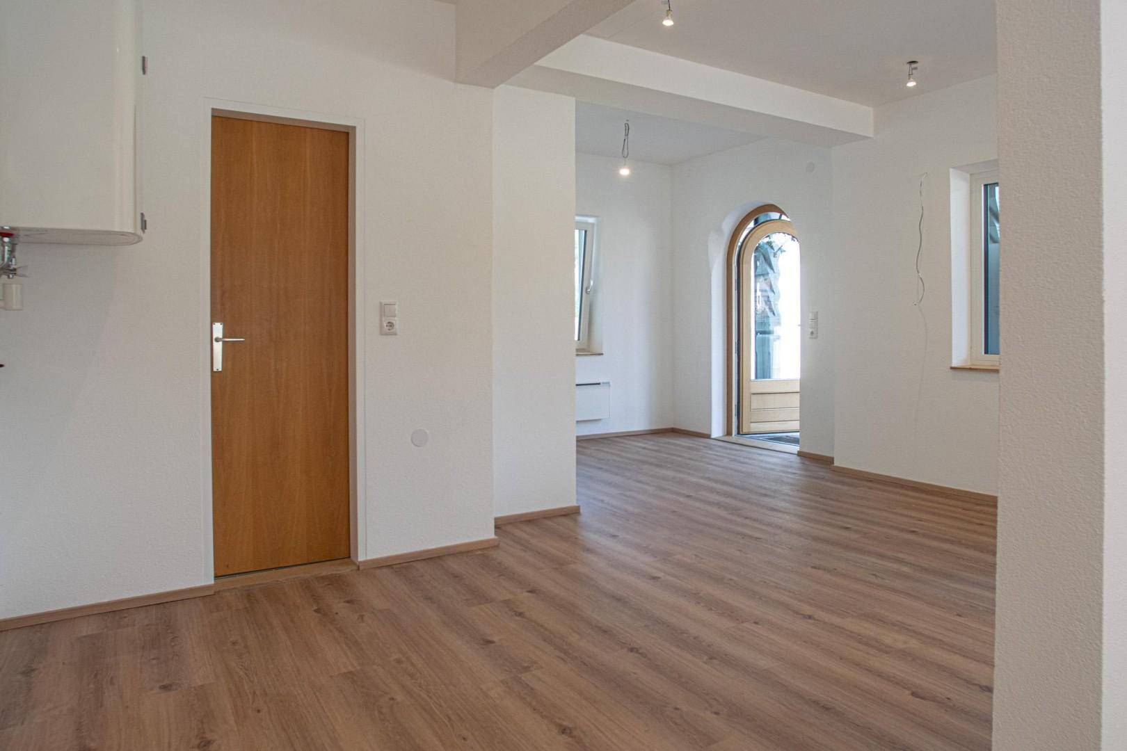Heller Innenraum mit Holzboden, weiß gestrichenen Wänden und einer Holztür.