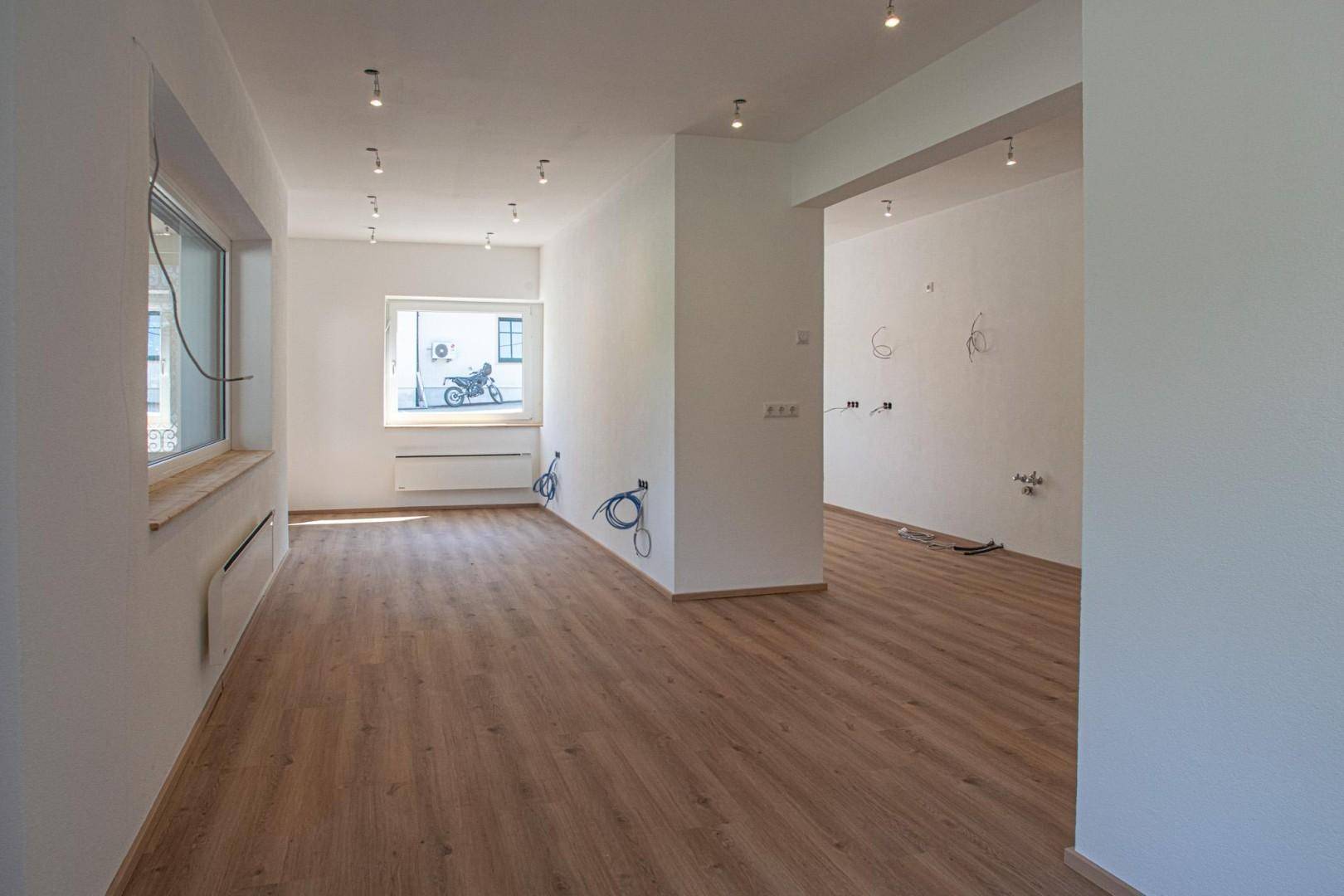 Geräumiger, heller Innenraum mit Laminatboden, weißen Wänden und sichtbaren Elektroinstallationen.