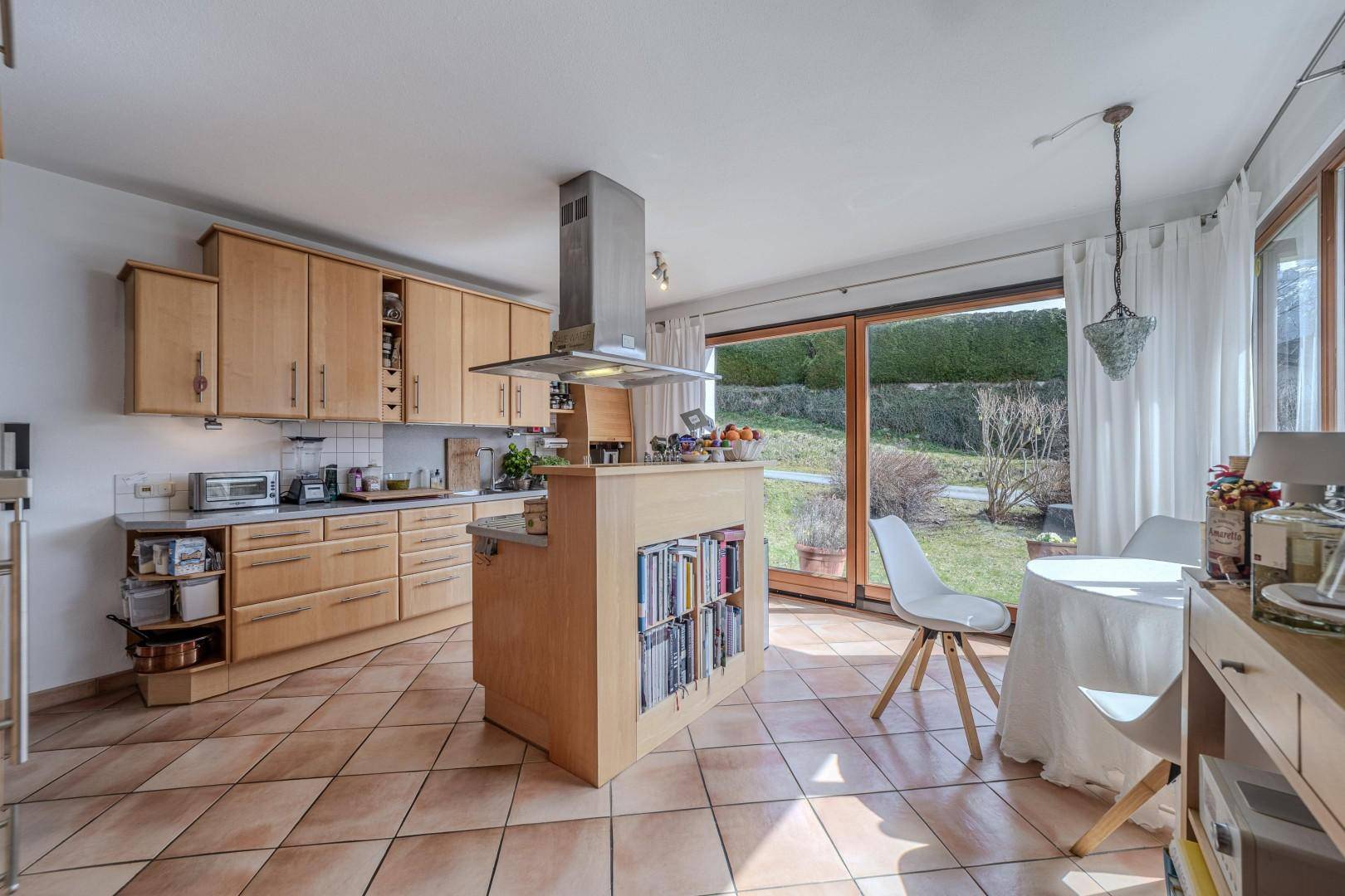 Helle Küche mit Holzschränken, Fliesenboden und Zugang zum Gartenbereich.