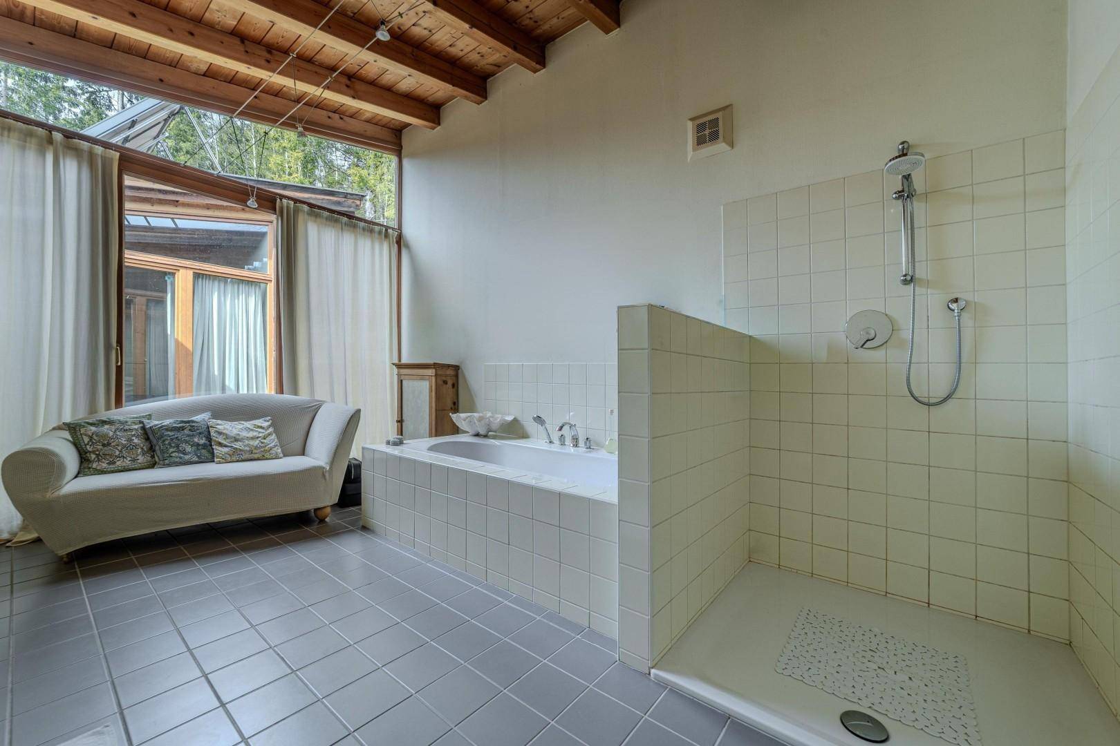 Helles Badezimmer mit Badewanne, Dusche und großem Fenster mit Blick ins Grüne.