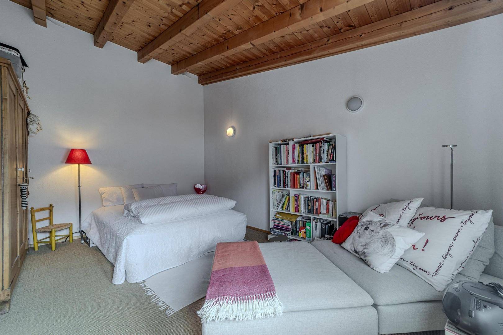 Geräumiges Schlafzimmer mit Holzbalkendecke, Bett und Bücherregal.