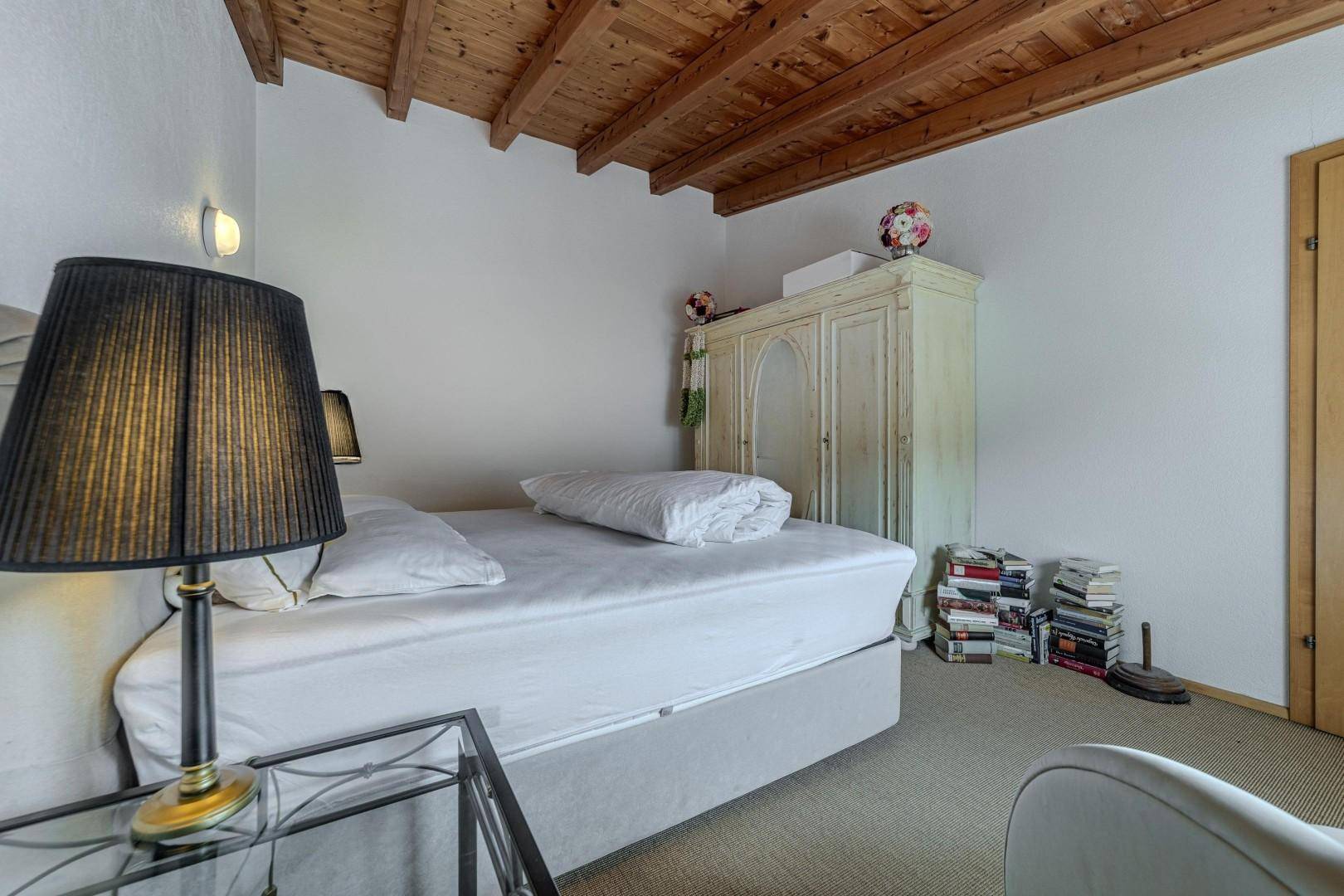 Schlafzimmer mit Holzbalkendecke, Einzelbett und antikem Kleiderschrank.