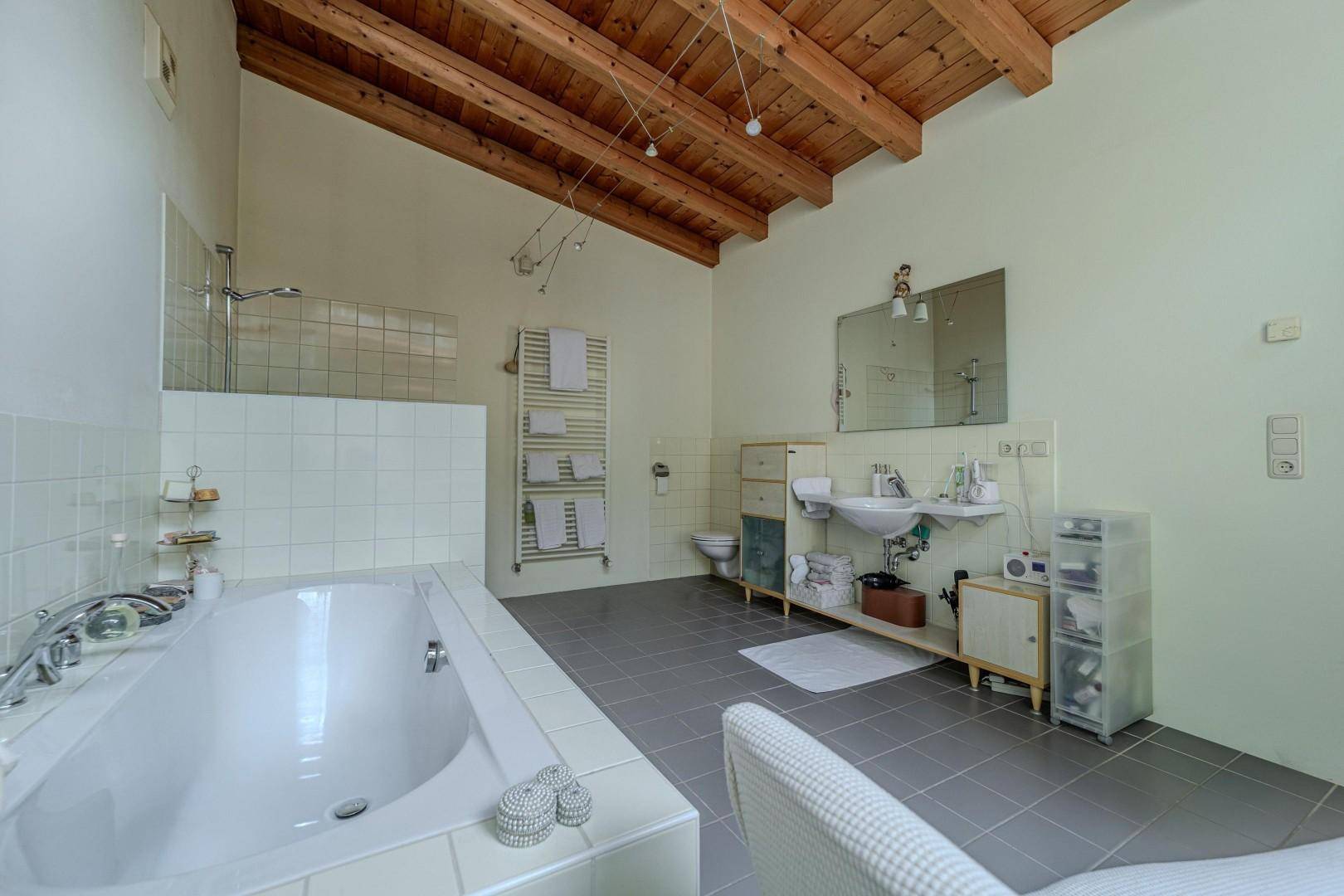Geräumiges Badezimmer mit Badewanne, Dusche, Doppelwaschbecken und Holzbalkendecke.
