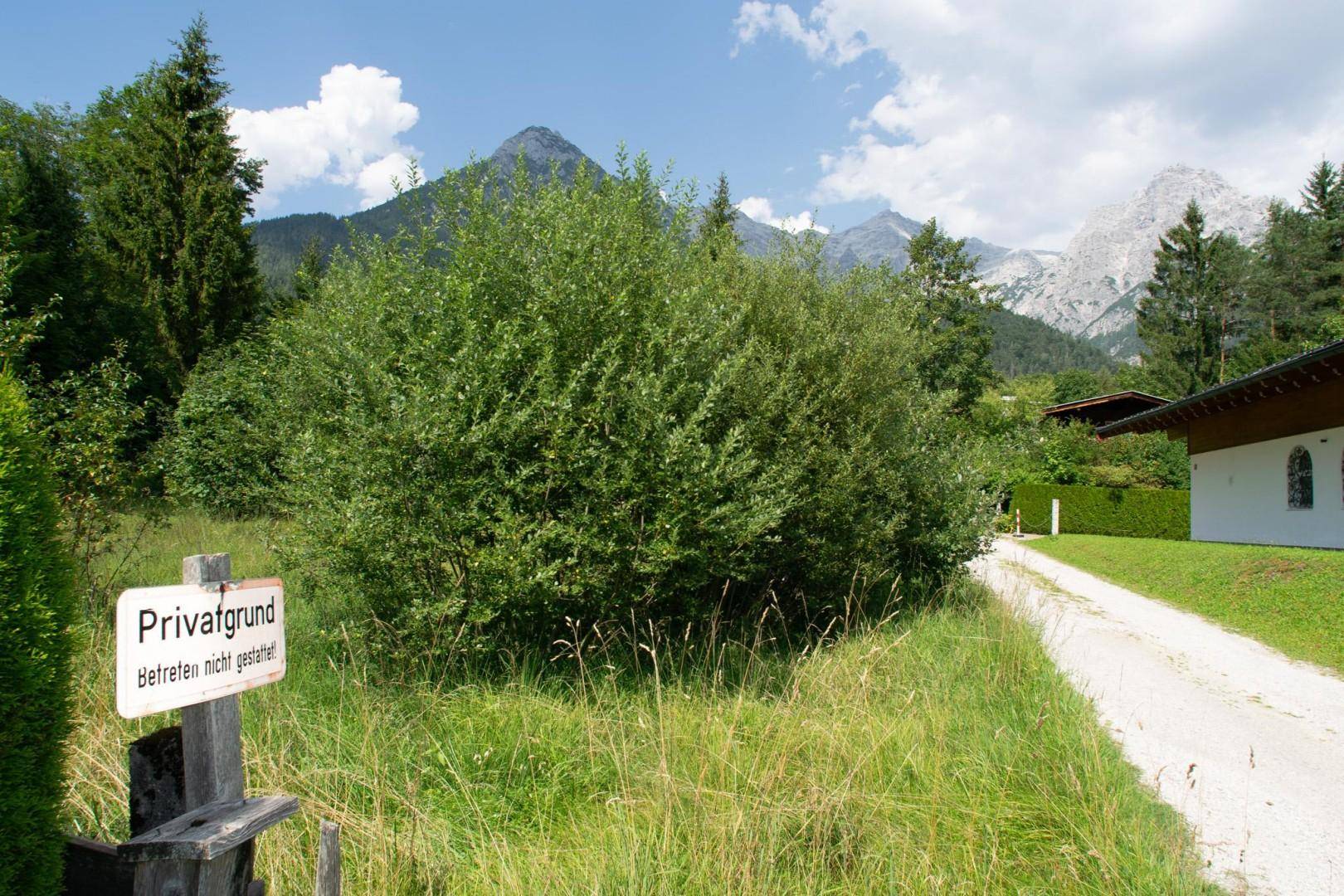 Weitläufige Grünfläche mit Schotterweg, umgeben von Bäumen und mit Bergblick im Hintergrund.
