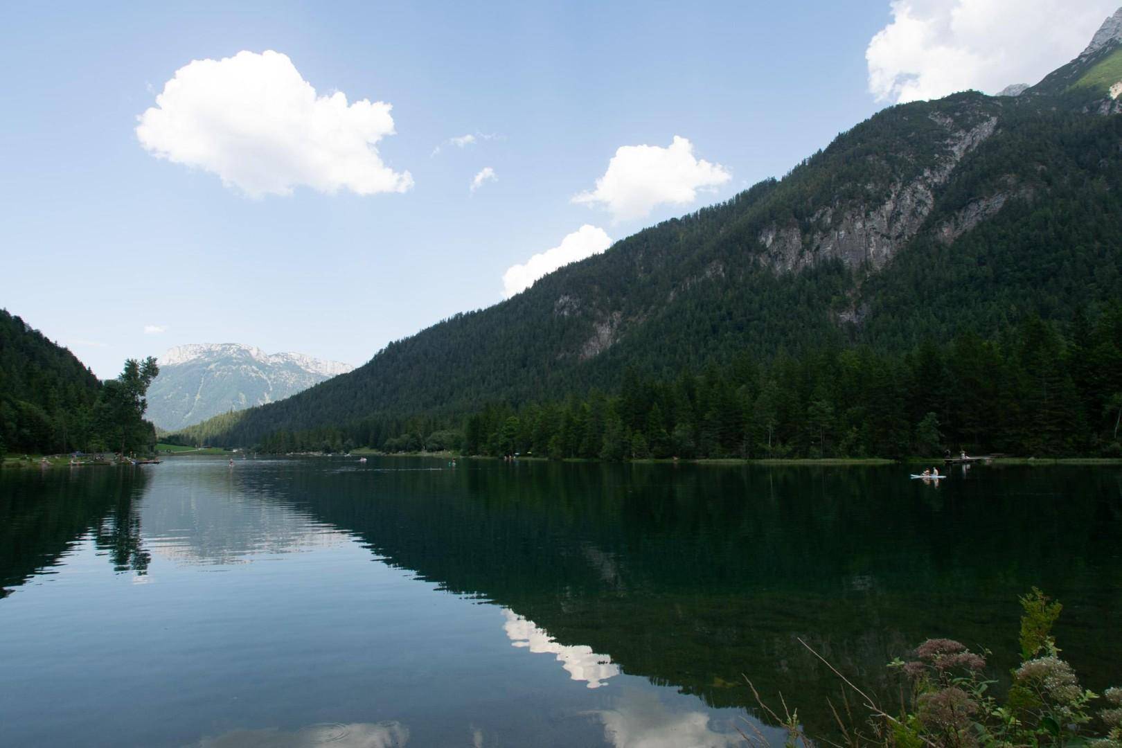 Malerischer Bergsee umgeben von bewaldeten Bergen unter einem klaren blauen Himmel.