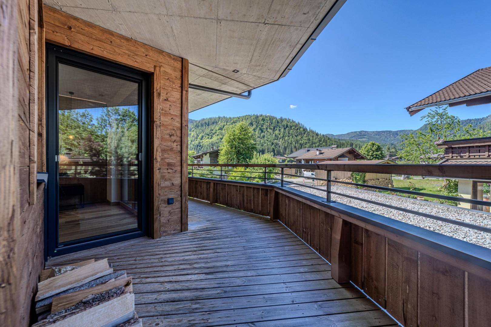 Langer Holzbalkon mit Holzstapel und Blick auf die grünen Berge und Häuser.