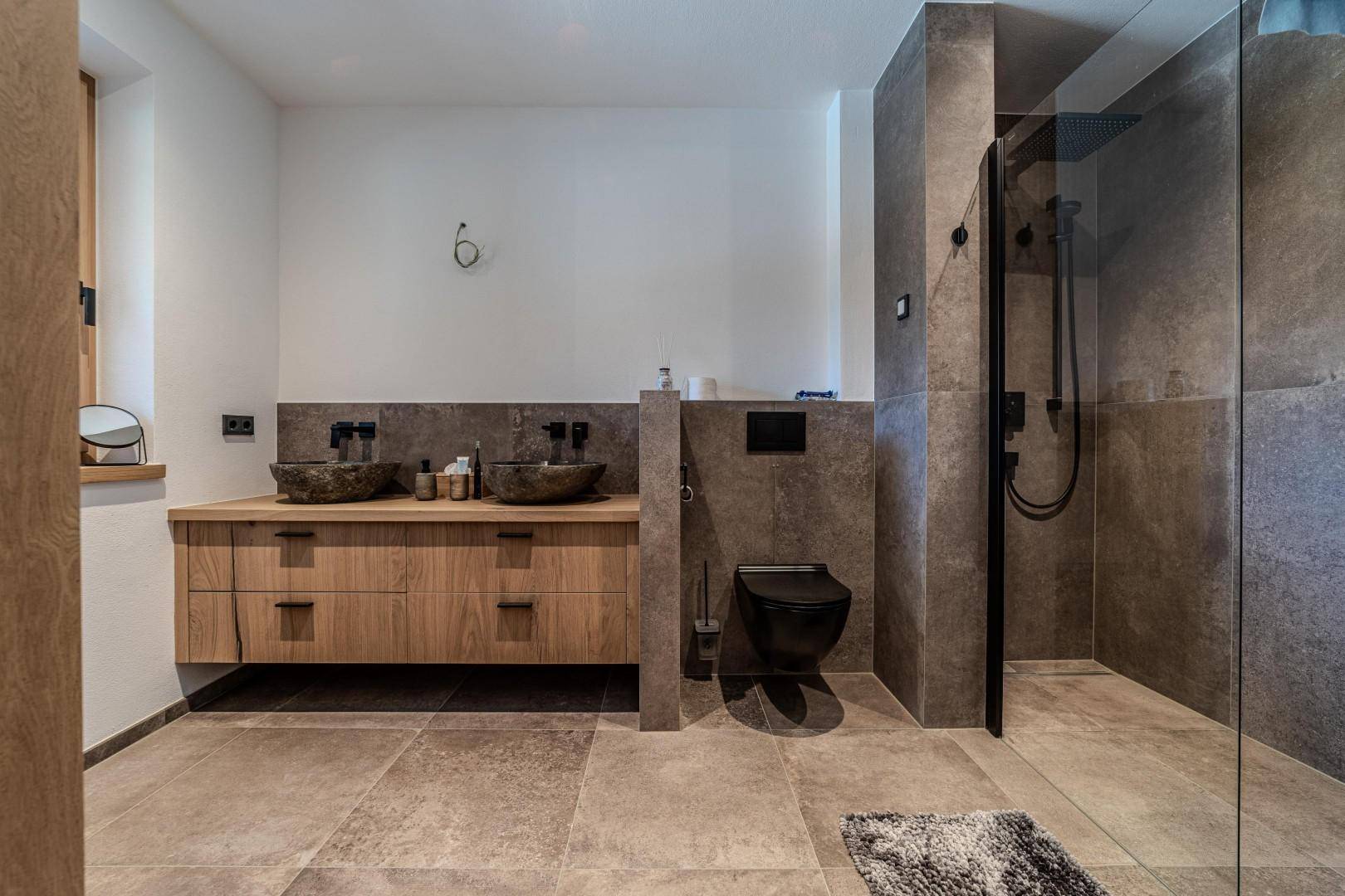Modernes Badezimmer mit Doppelwaschbecken, begehbarer Dusche und dunklen Fliesen.