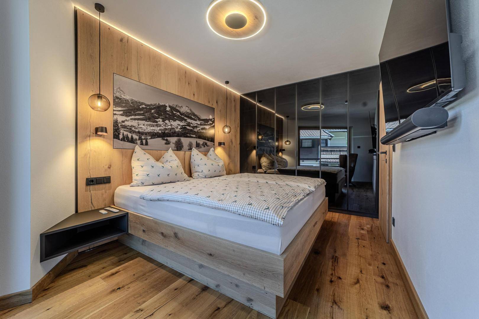 Schlafzimmer mit Holzboden, Spiegelschränken und modernem Doppelbett.