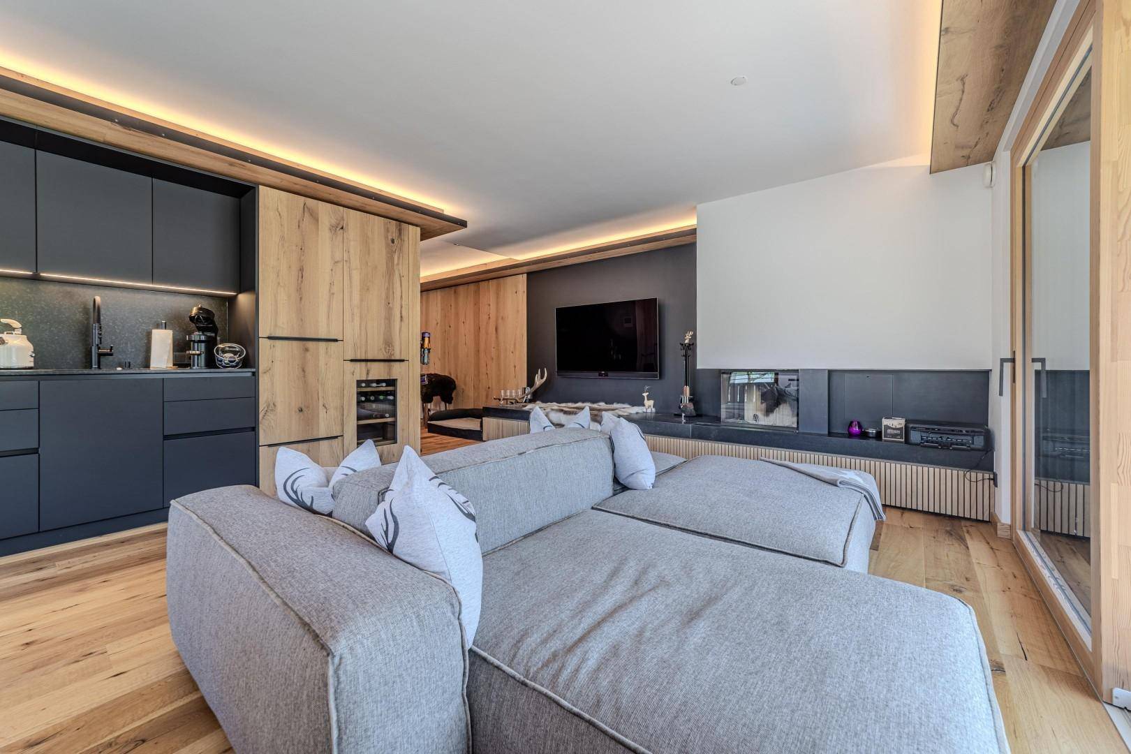 Moderner Wohnbereich mit integrierter Küche, Kamin und Holzakzenten.