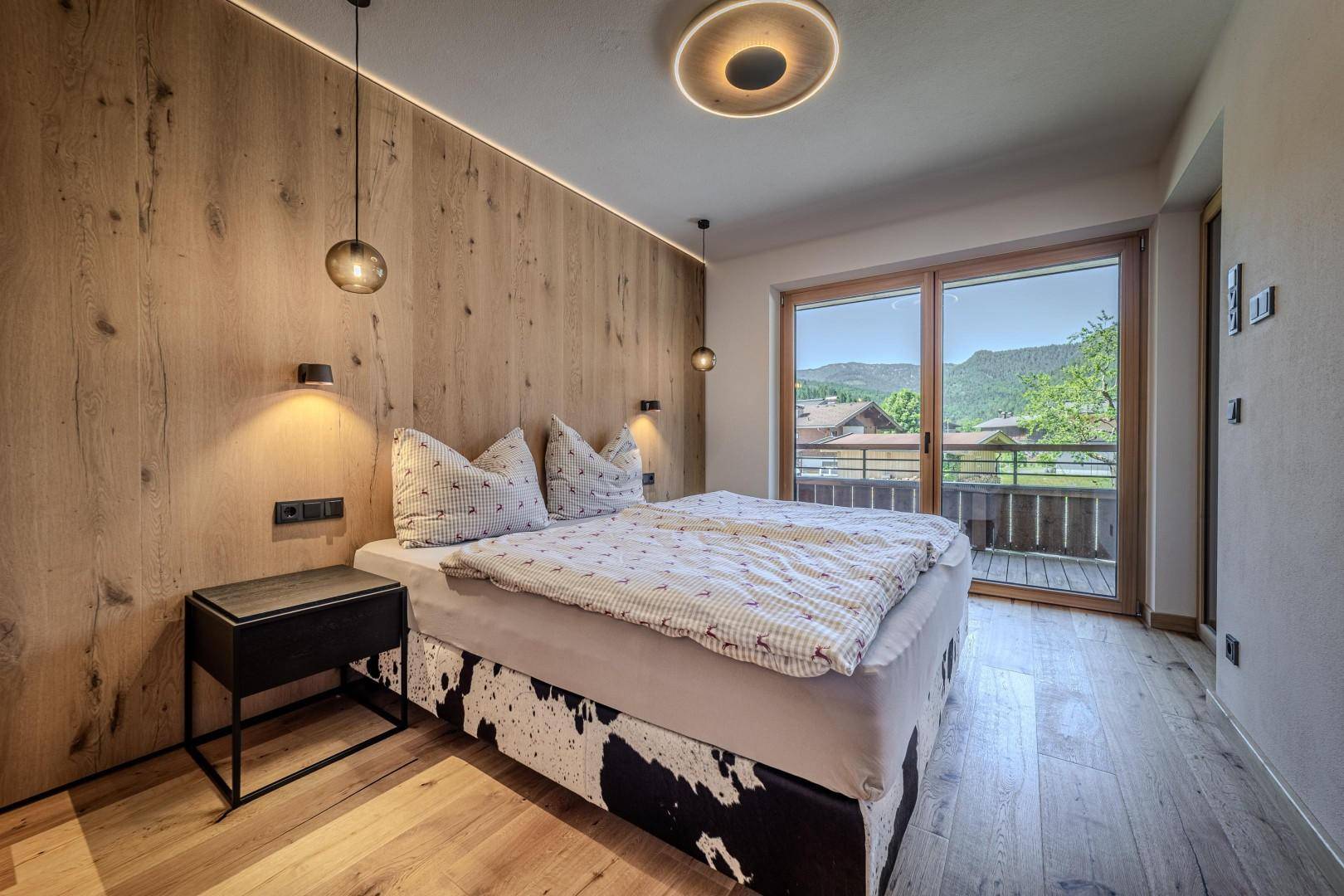 Gemütliches Schlafzimmer mit Holzwand, Doppelbett und Balkonzugang mit Bergblick.
