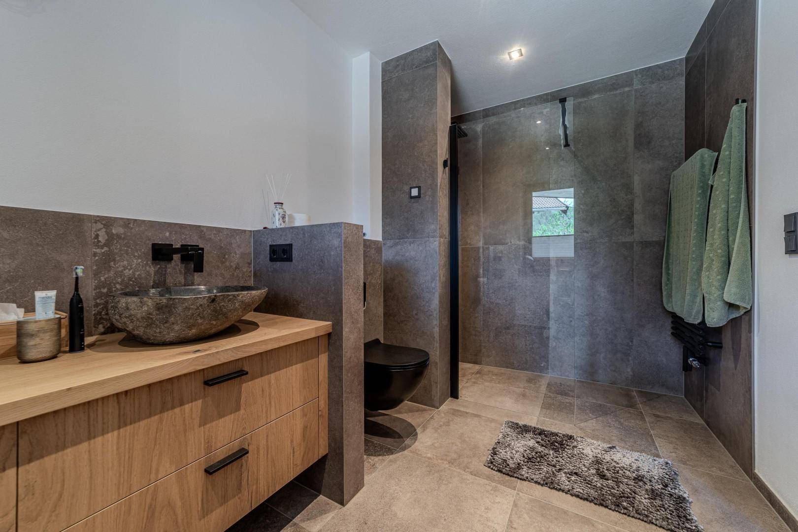 Elegantes Badezimmer mit Steinfliesen, Holzwaschtisch und großer begehbarer Dusche.