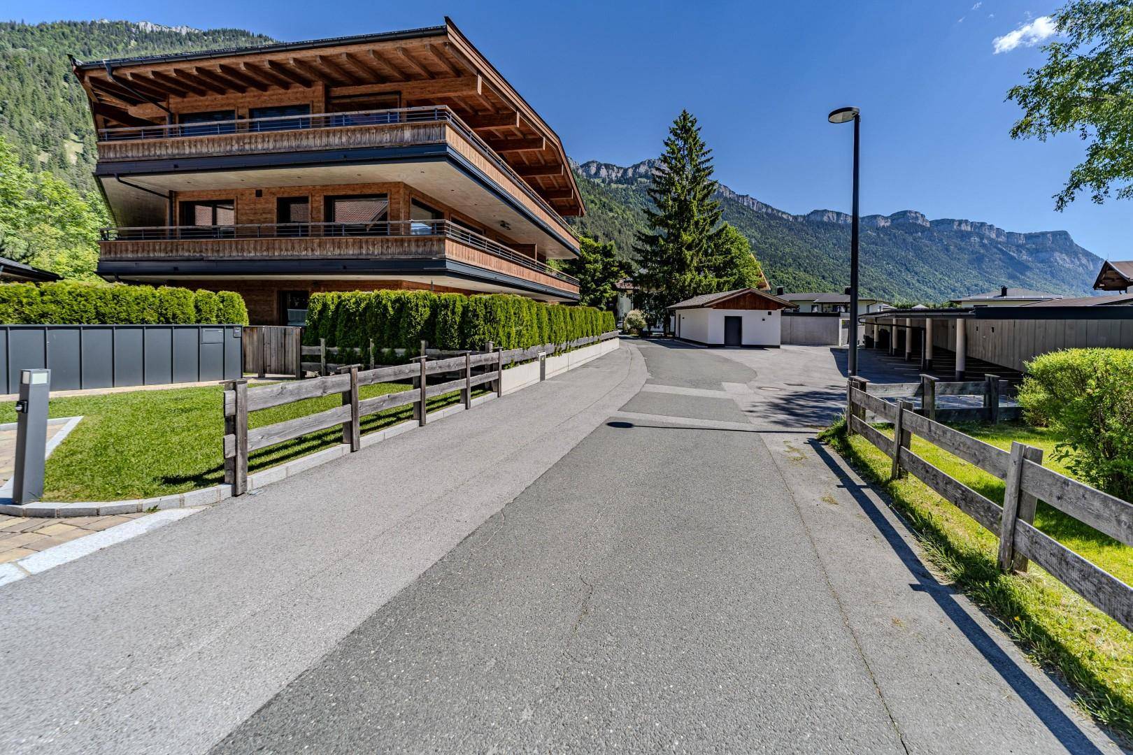 Modernes Mehrfamilienhaus mit Holzfassade und Balkonen, eingebettet in eine alpine Berglandschaft.
