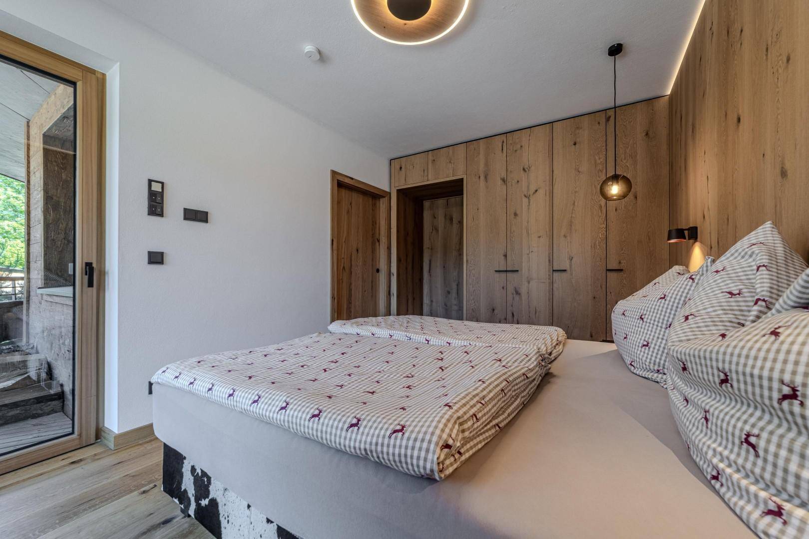 Helles Schlafzimmer mit Holzboden, Doppelbett und Zugang zu einem Außenbereich.