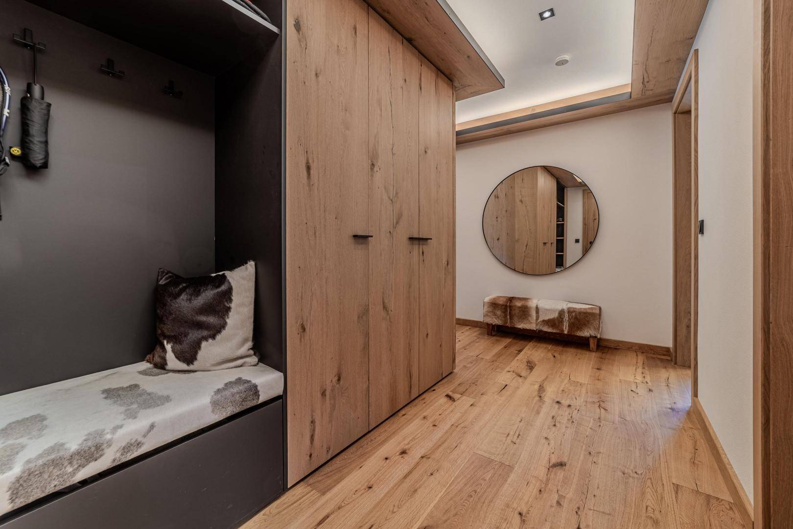 Heller Flur mit Holzboden, runden Spiegel und Sitzbank mit Fellkissen.
