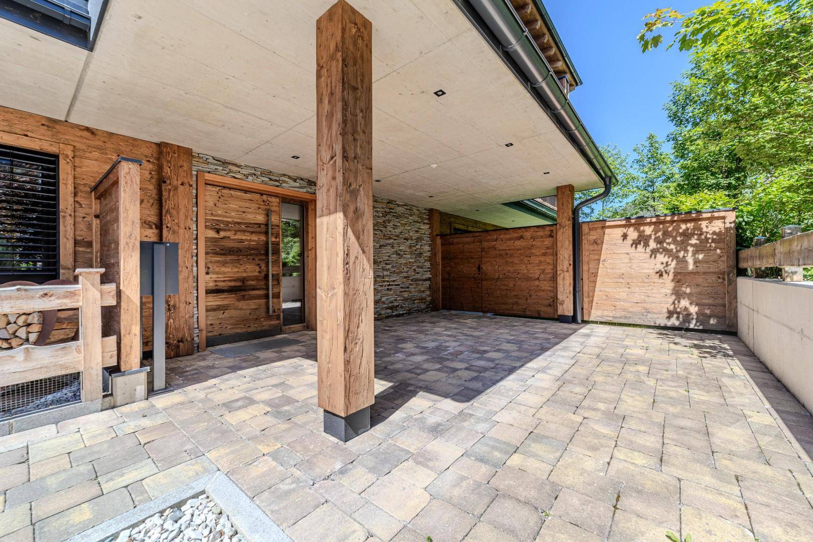 Überdachter Eingangsbereich oder Carport mit Holzelementen und Steinpflasterung, umgeben von natürlicher Architektur.