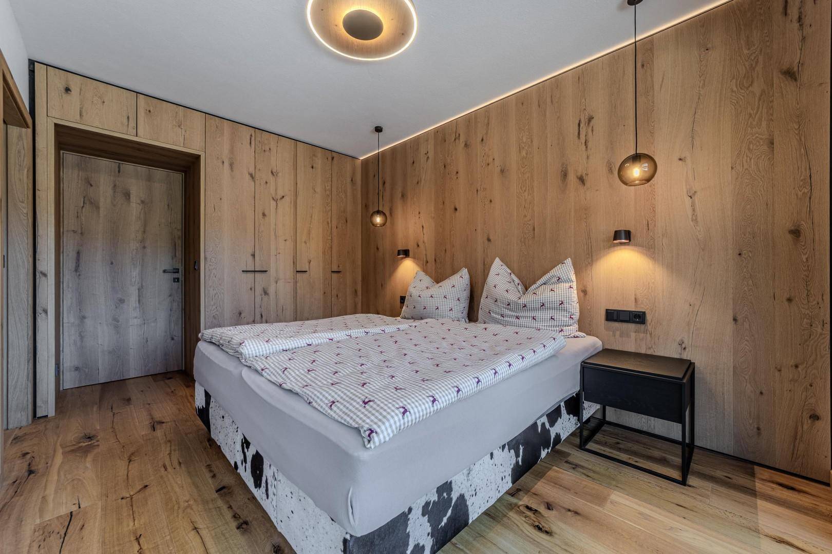 Schlafzimmer mit Holzwand, integrierten Schränken und modernem Doppelbett.