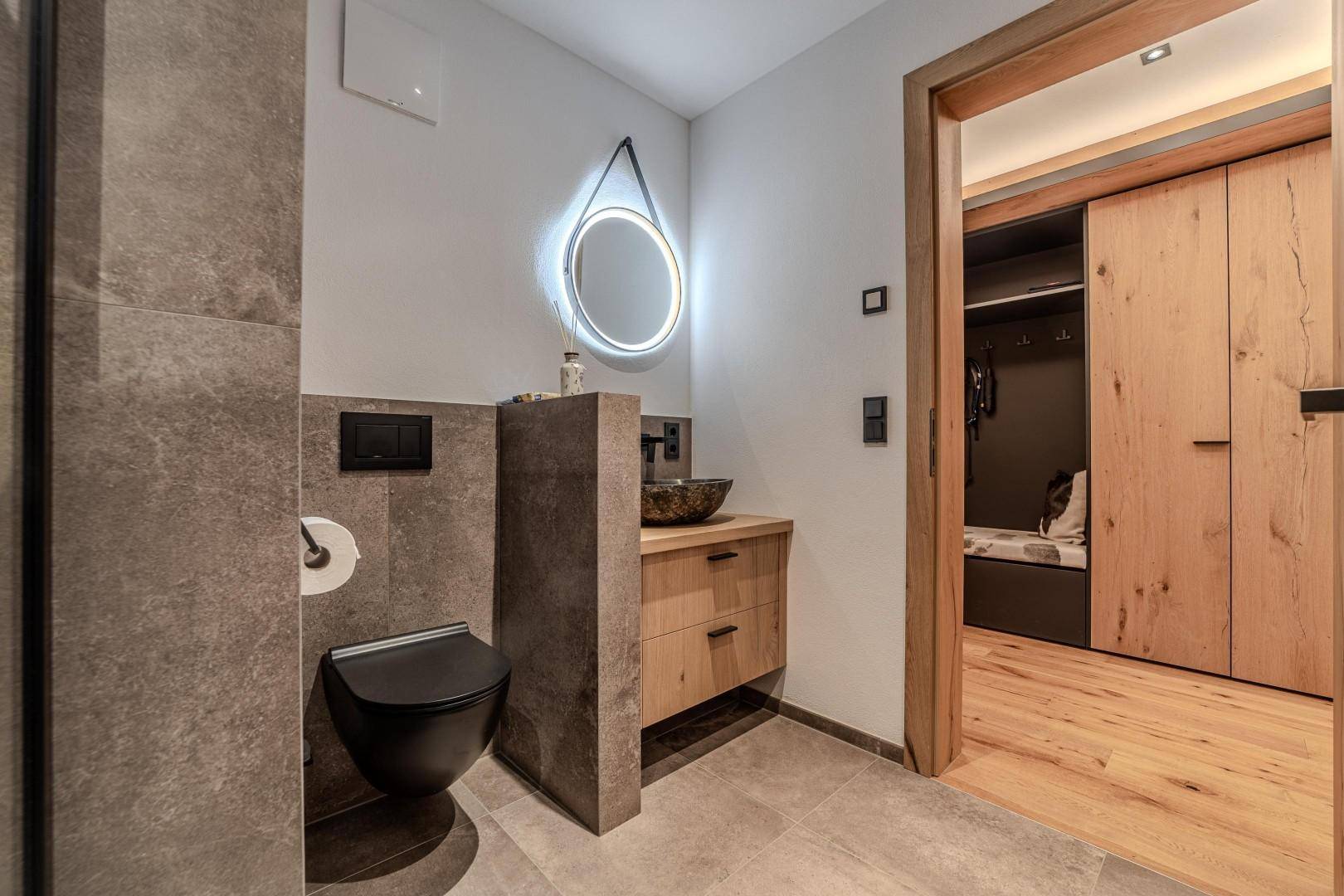 Gäste-WC mit modernem Design, beleuchtetem Spiegel und Holzelementen.