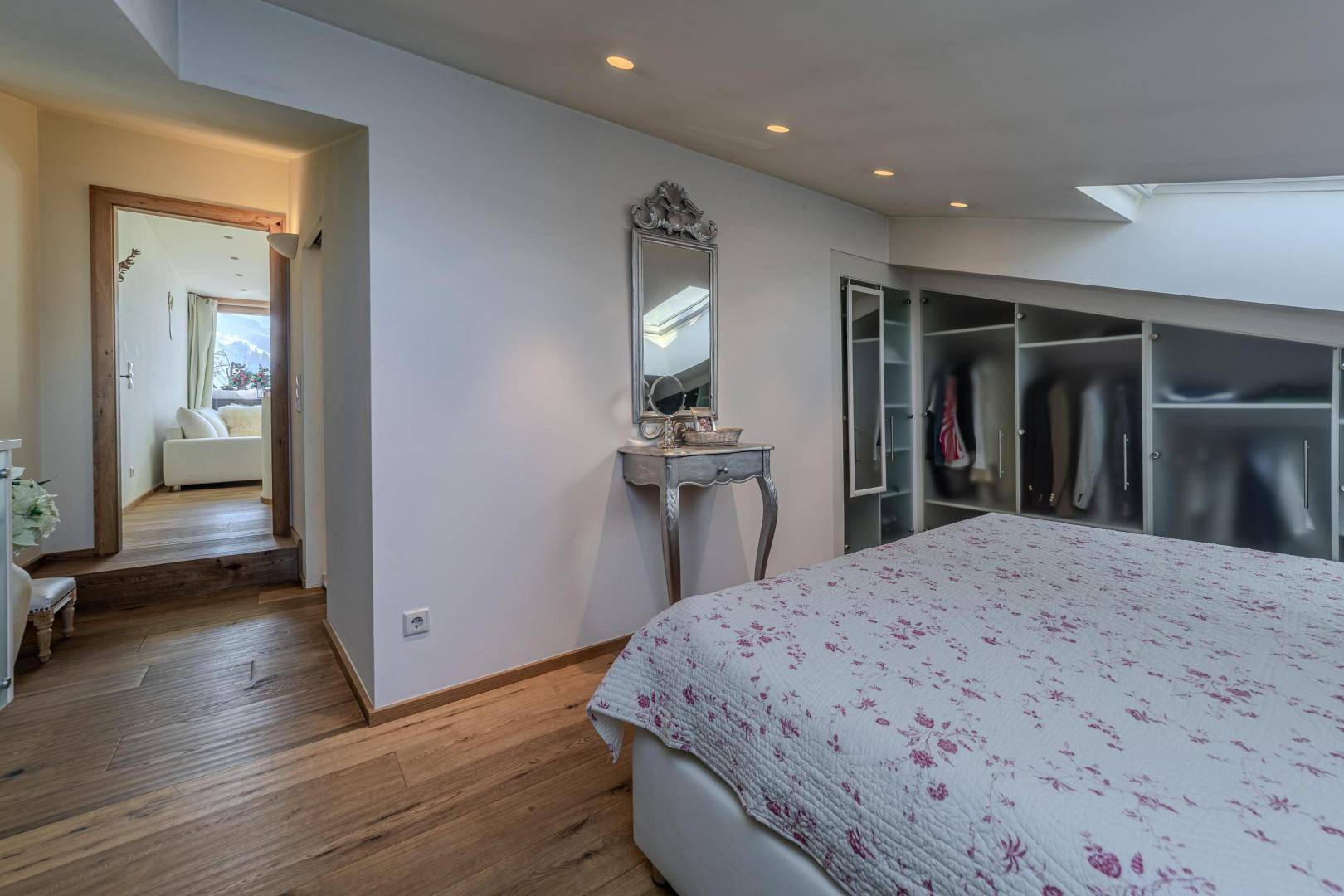 Schlafzimmer mit Holzboden und Zugang zu einem weiteren Raum, ergänzt durch einen eleganten Schminktisch.