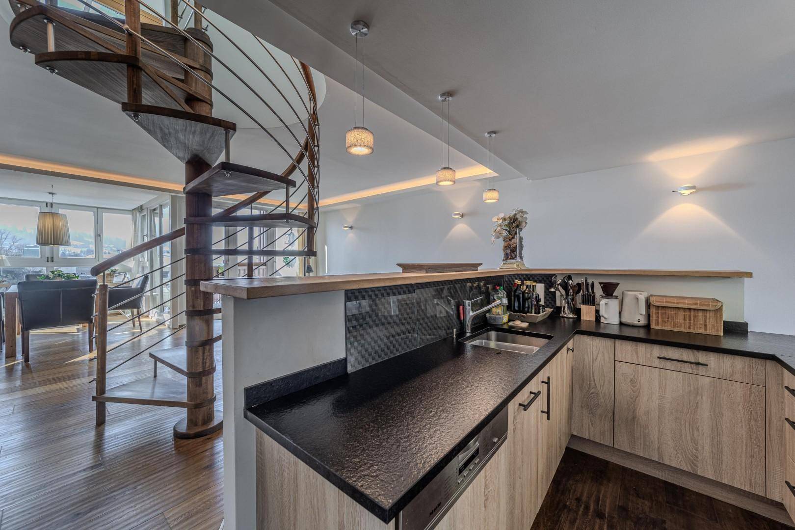 Funktionale Küche mit Holzschränken, schwarzer Arbeitsplatte und Blick auf den Wohnbereich.