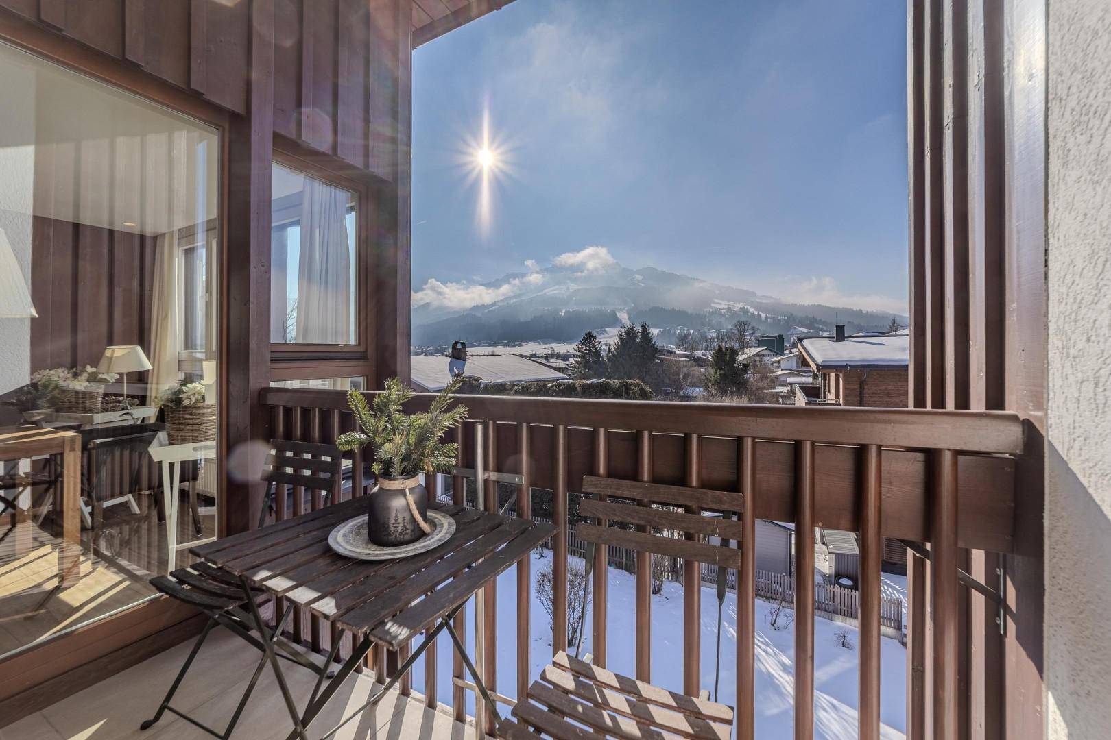 Sonniger Balkon mit Holzboden, Sitzgelegenheiten und atemberaubendem Blick auf die verschneiten Berge.