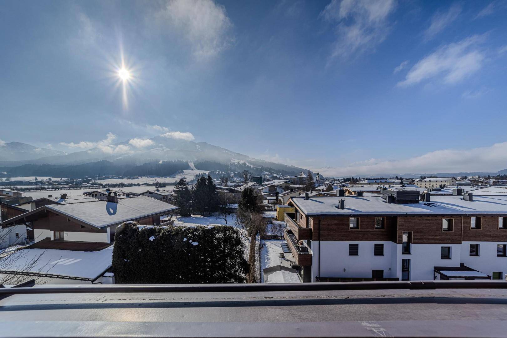 Panoramablick über eine verschneite Stadt und die umliegenden Berge an einem sonnigen Wintertag.